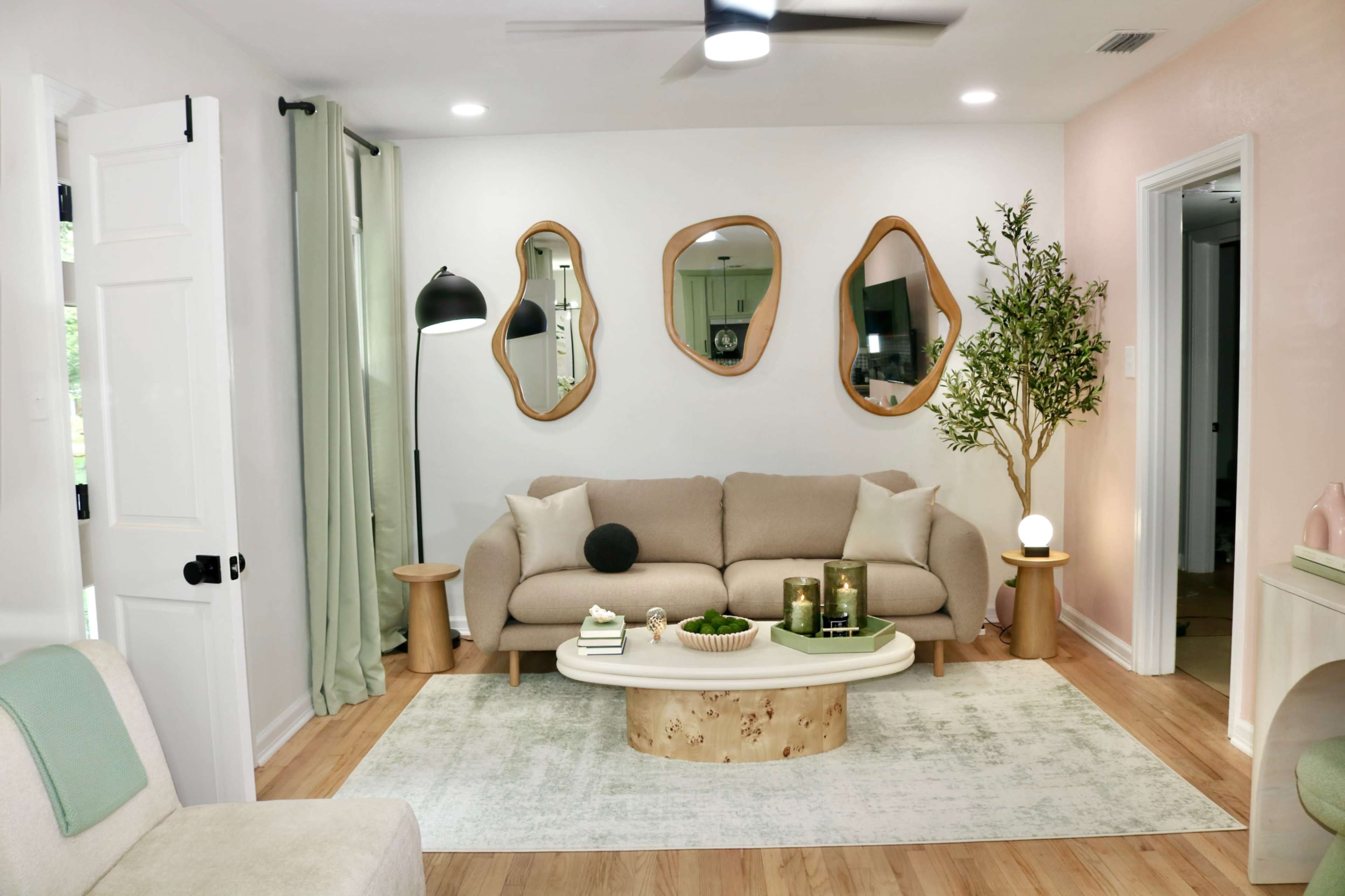 The image shows a modern living room with a light-colored sofa, decorative mirrors on the wall, a small wooden coffee table, and a plant in the corner.