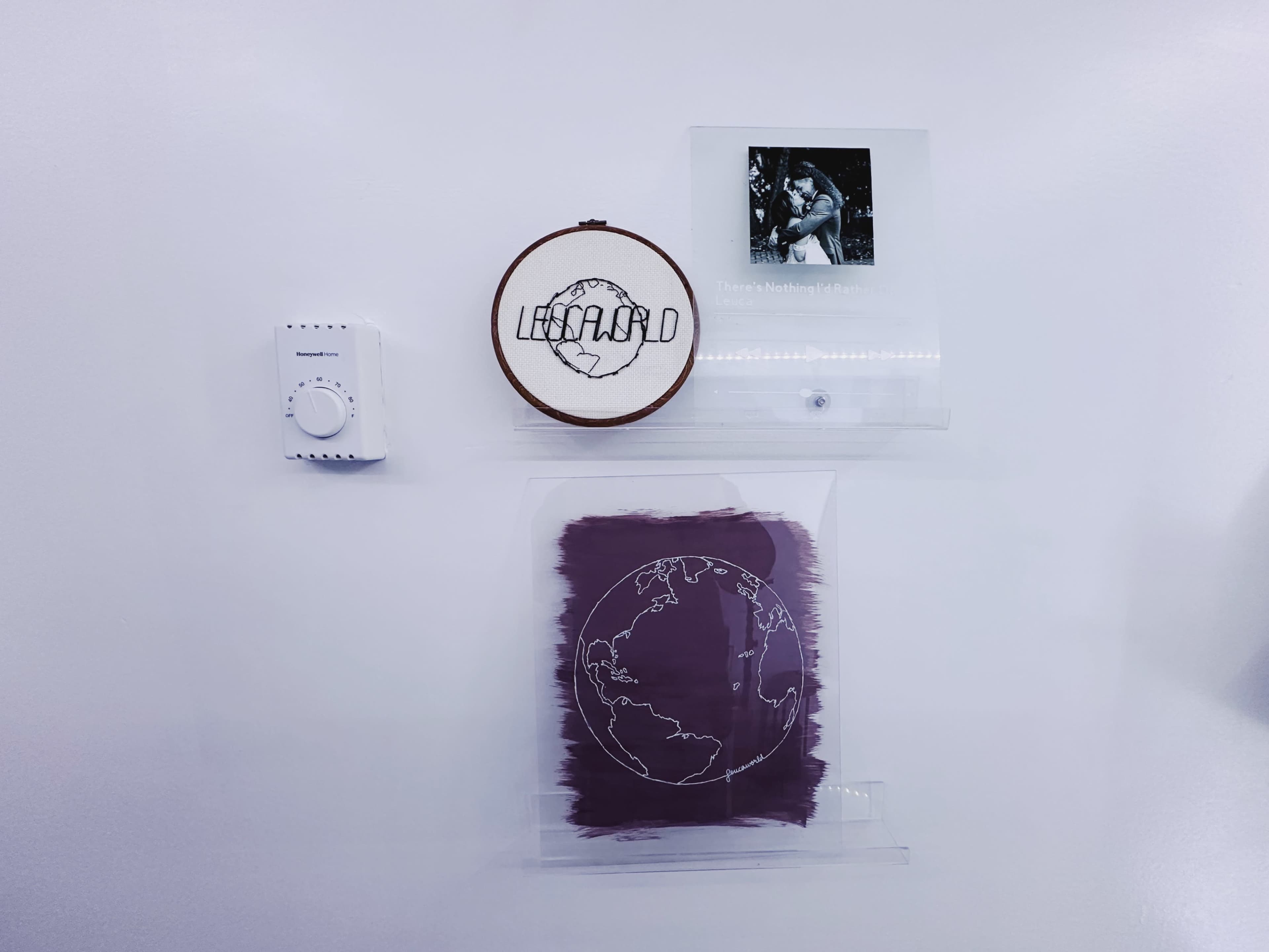 A wall display featuring an embroidered circle with the word "LIVID," a photo in a clear frame, a switch, and a purple earth-themed illustration.