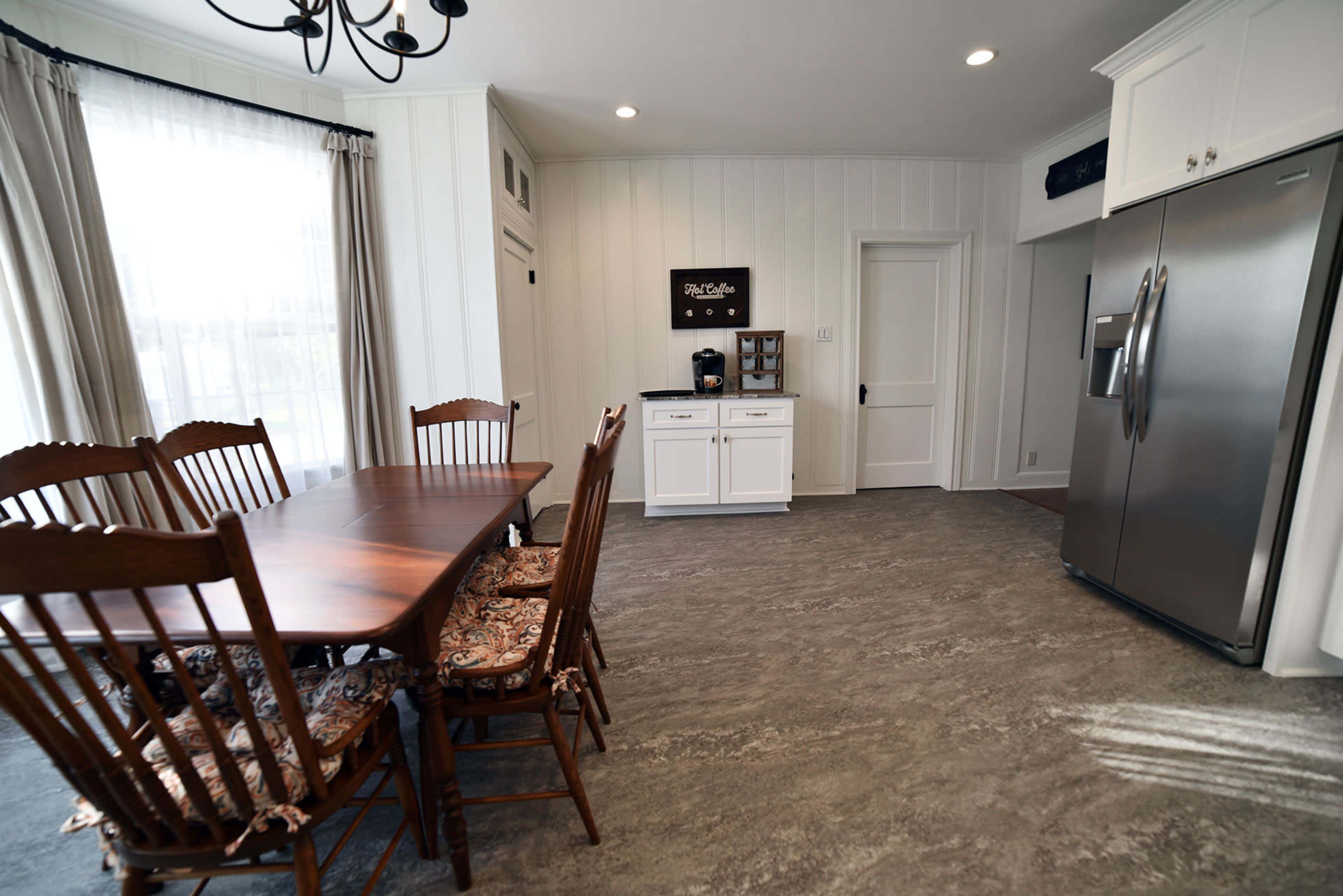 A dining area featuring a wooden table and chairs, with a white kitchen counter and silver refrigerator nearby.