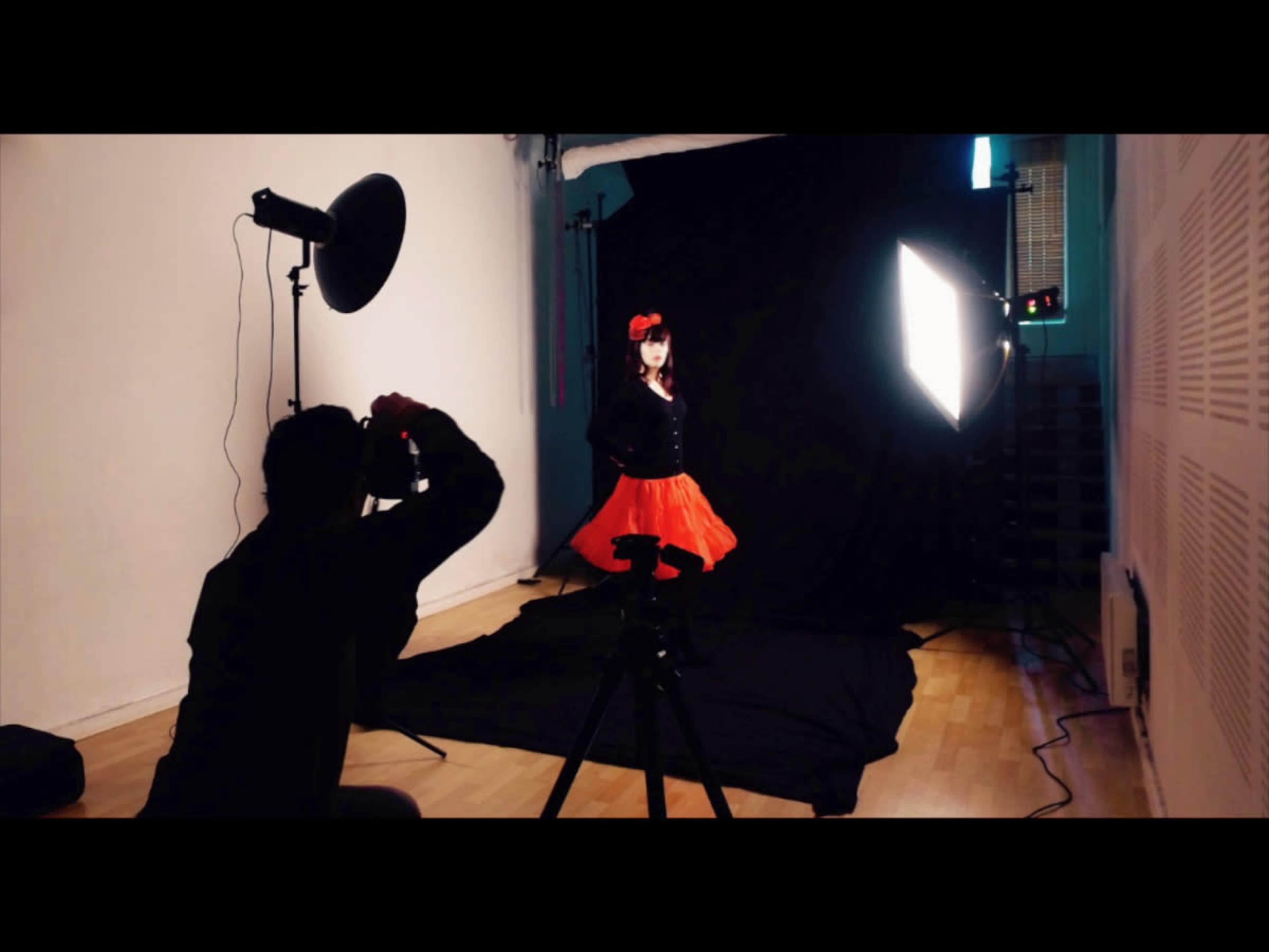 A photographer captures a portrait of a child in a red dress against a black backdrop in a studio setting.