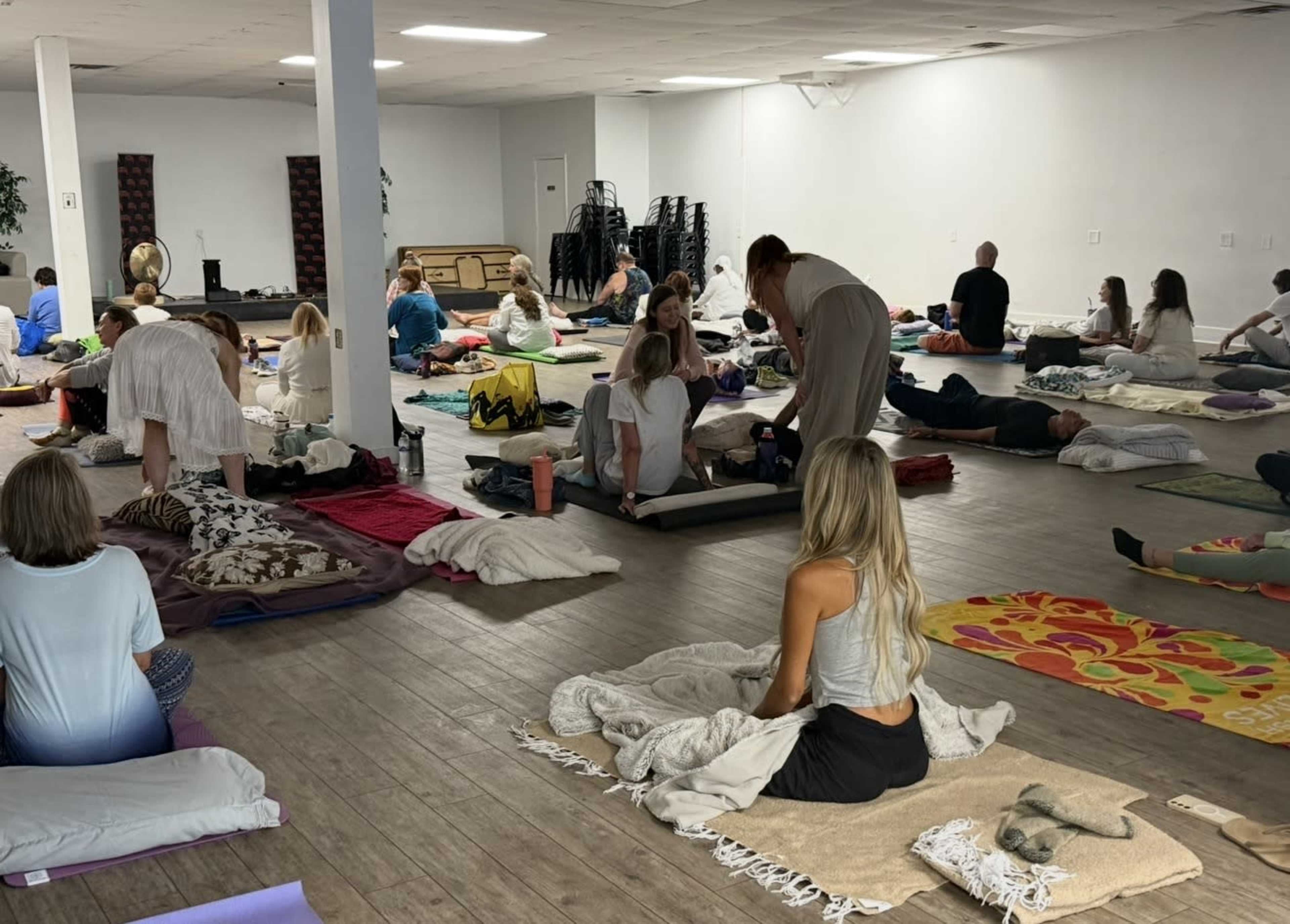 The image shows a spacious room filled with individuals lying on mats and cushions, participating in a wellness or meditation session.