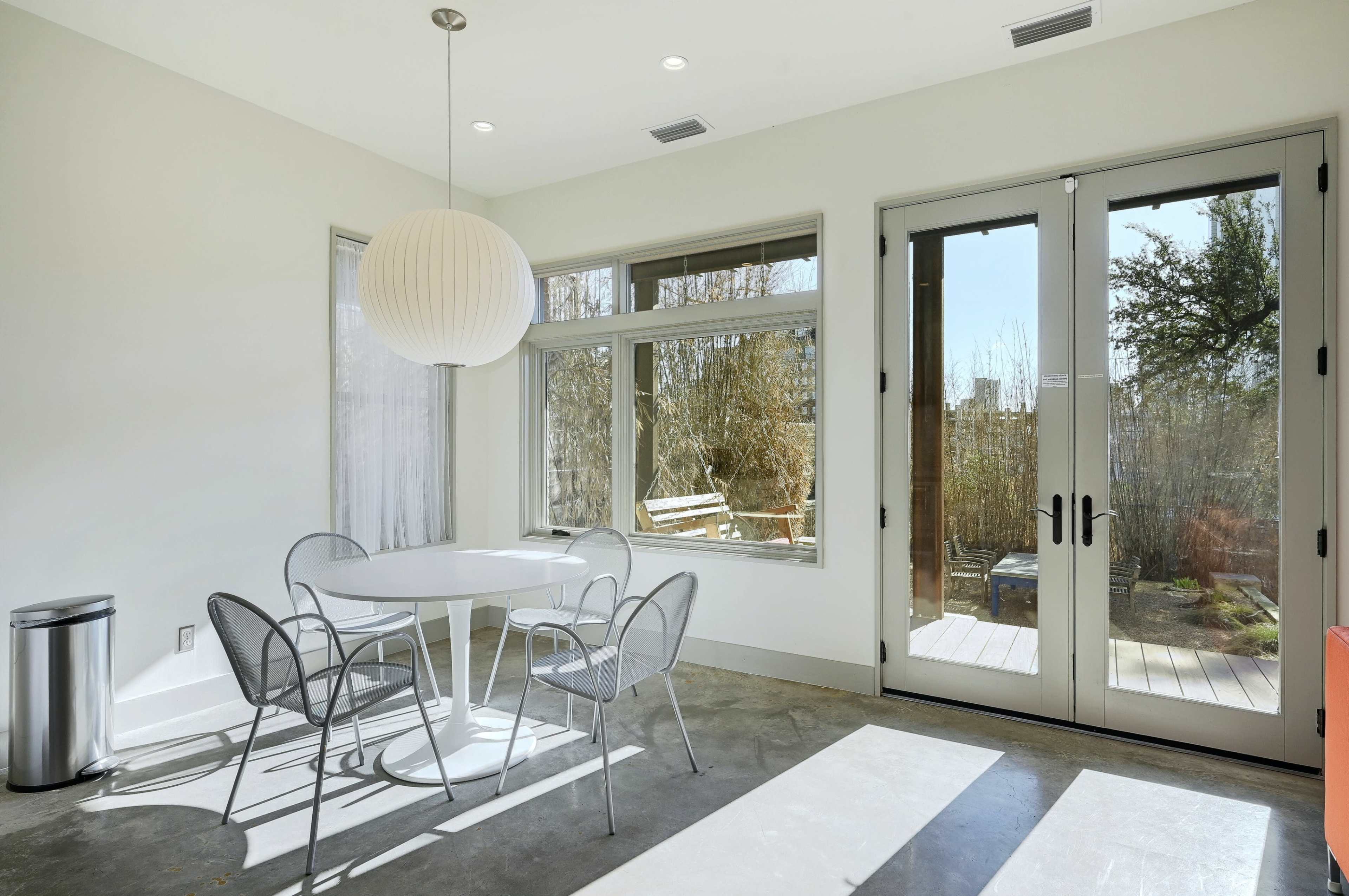 A dining area features a round table with four metal chairs and a large pendant light, alongside glass doors leading to an outdoor patio.
