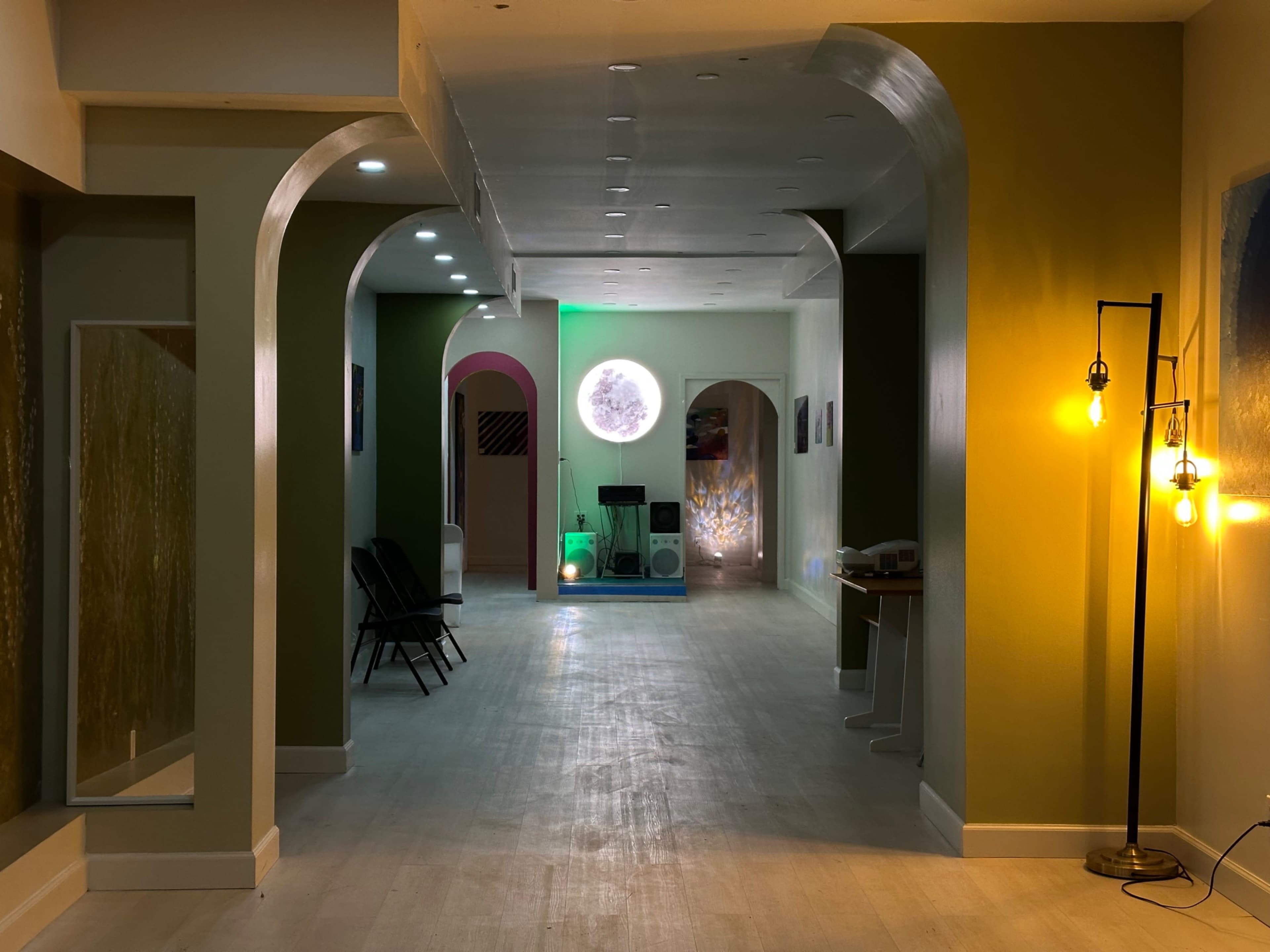 The image shows a spacious modern interior with archways, a circular light fixture at the end, and various seating arrangements along the walls.