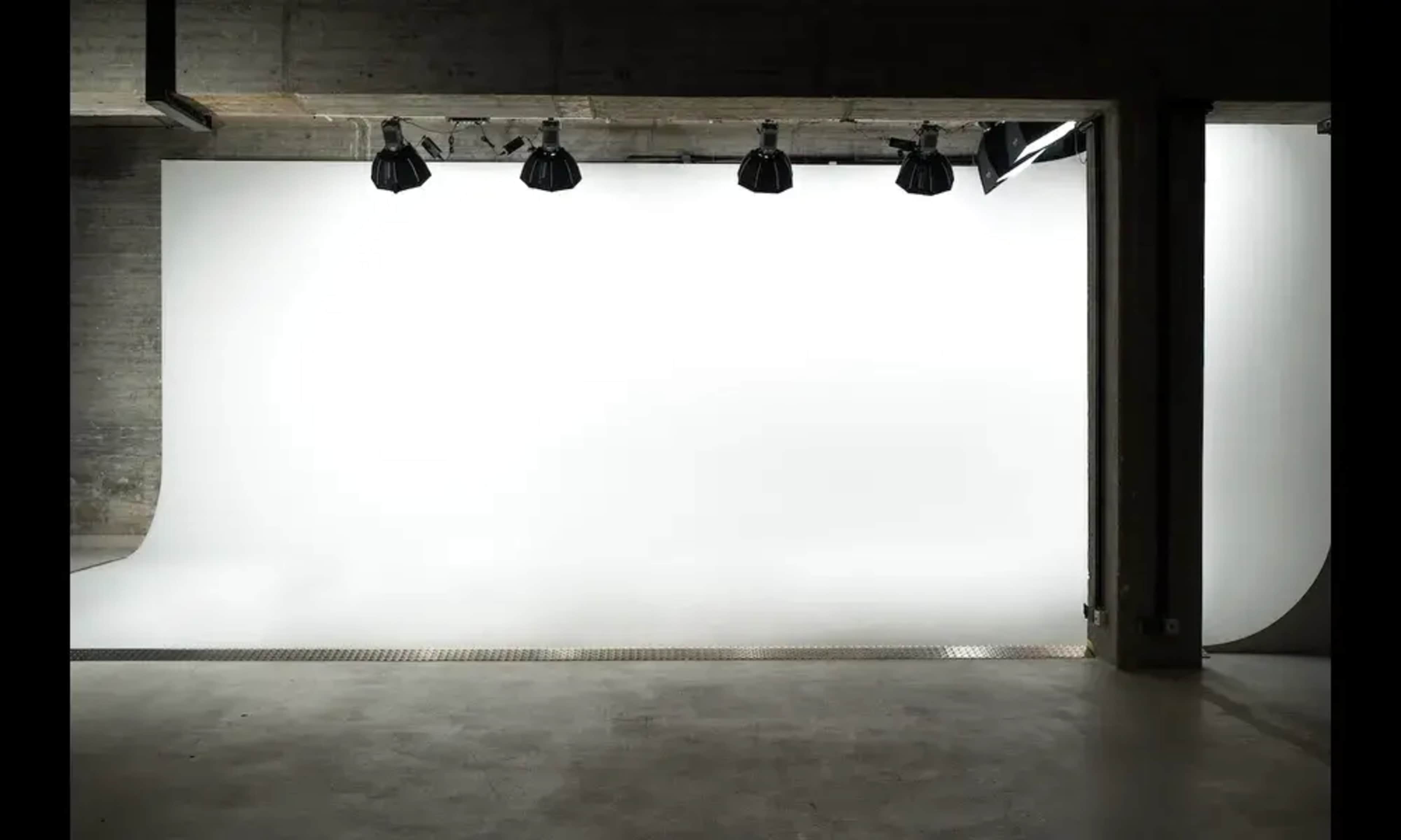 The image depicts a photography studio with a seamless white backdrop and overhead studio lights.