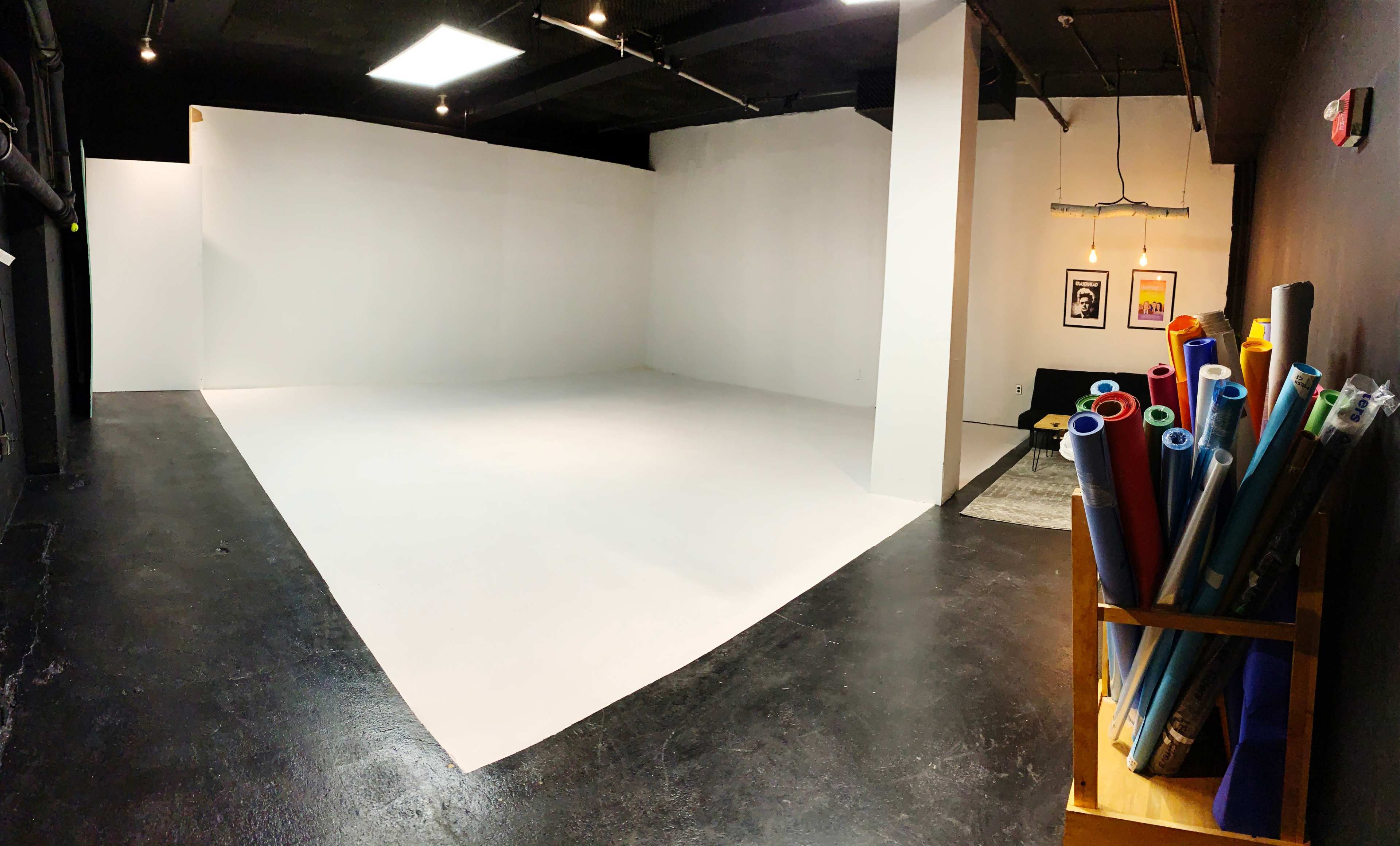 A spacious, minimalist studio with a large, white backdrop and a rack of colored rolls of paper on the right.