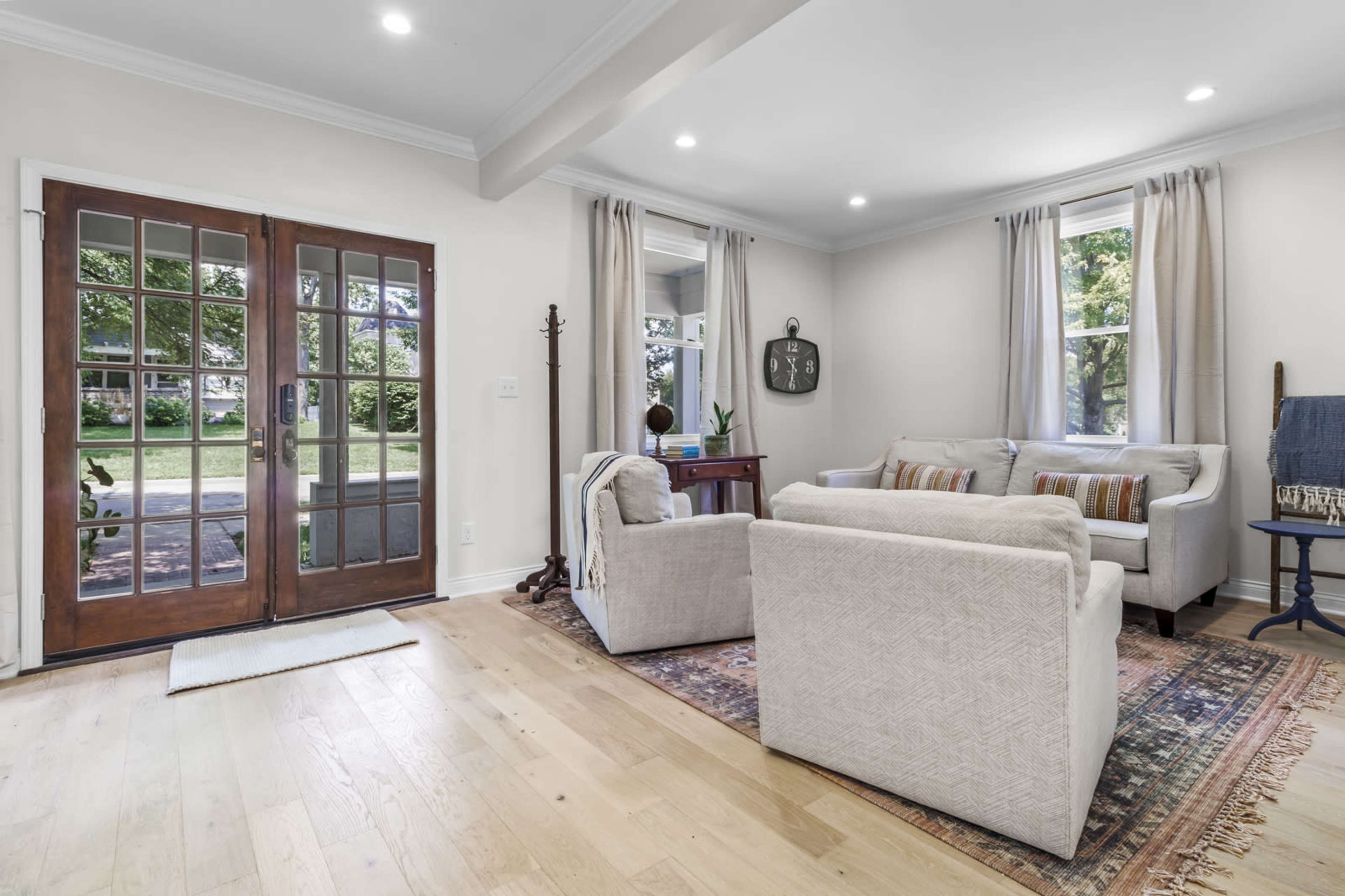 The scene shows a living room with two armchairs and a sofa arranged around a rug, with large windows and double doors leading to an outdoor area.