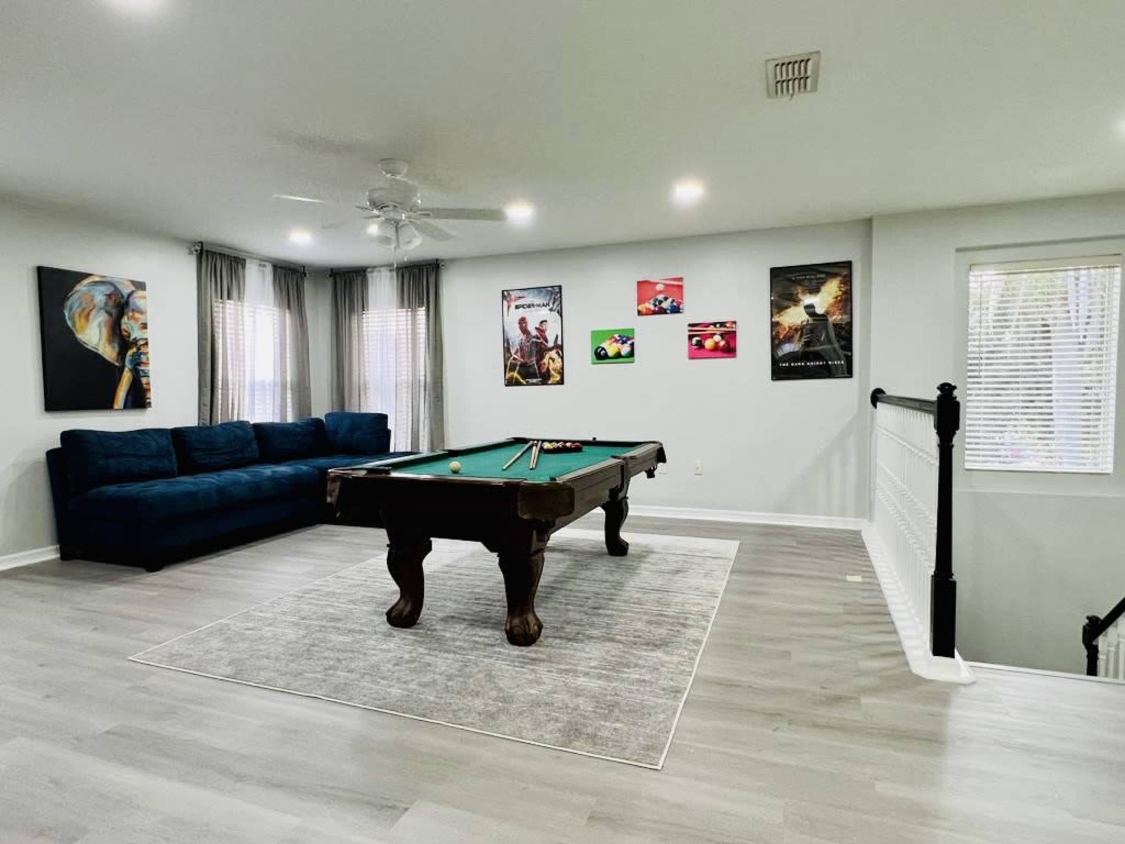 A modern game room with a pool table in the center, a blue couch against the wall, and colorful artwork hanging on the walls.