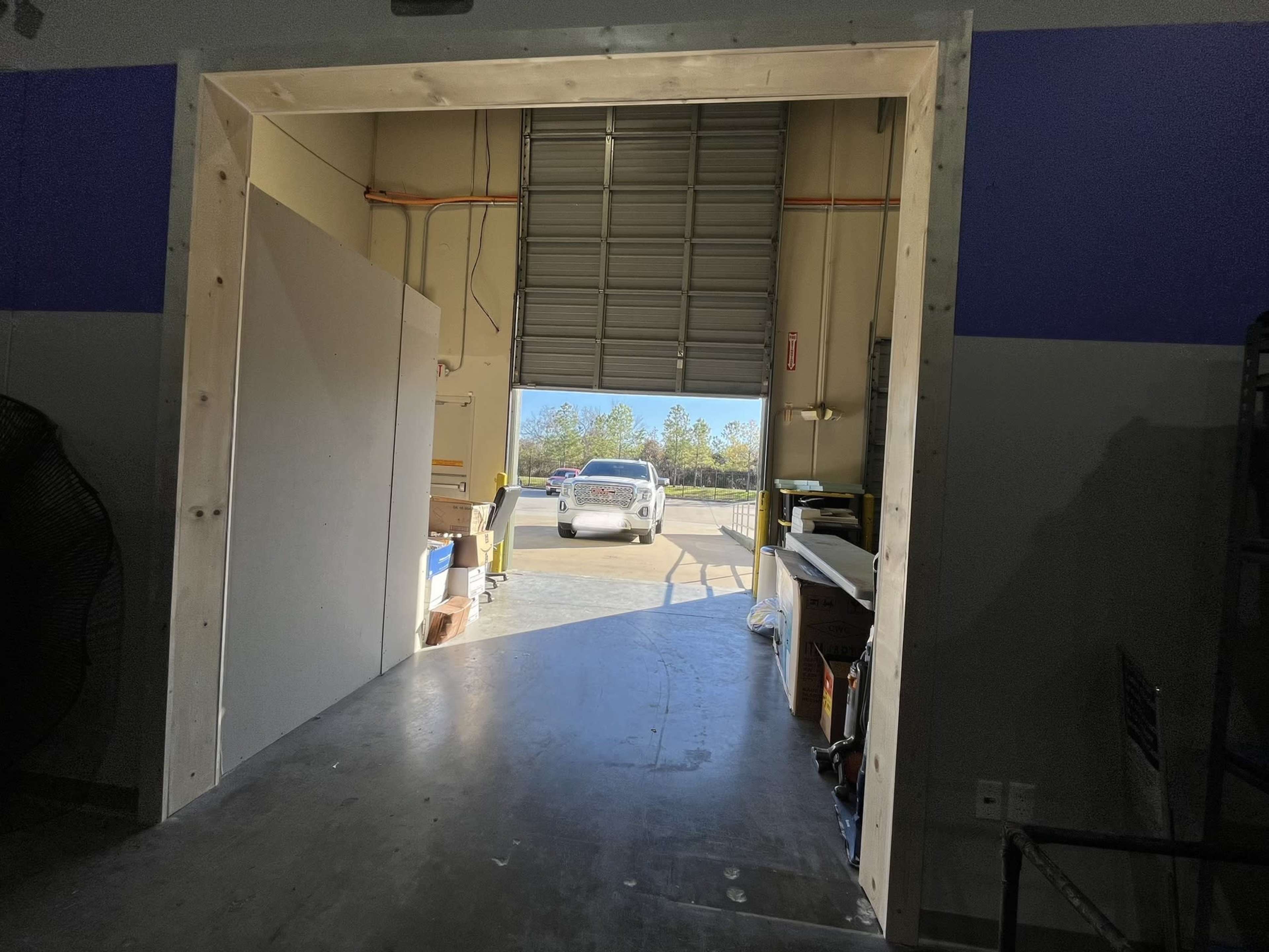 An open garage door leading to an outdoor area, with a car parked outside on a concrete surface.