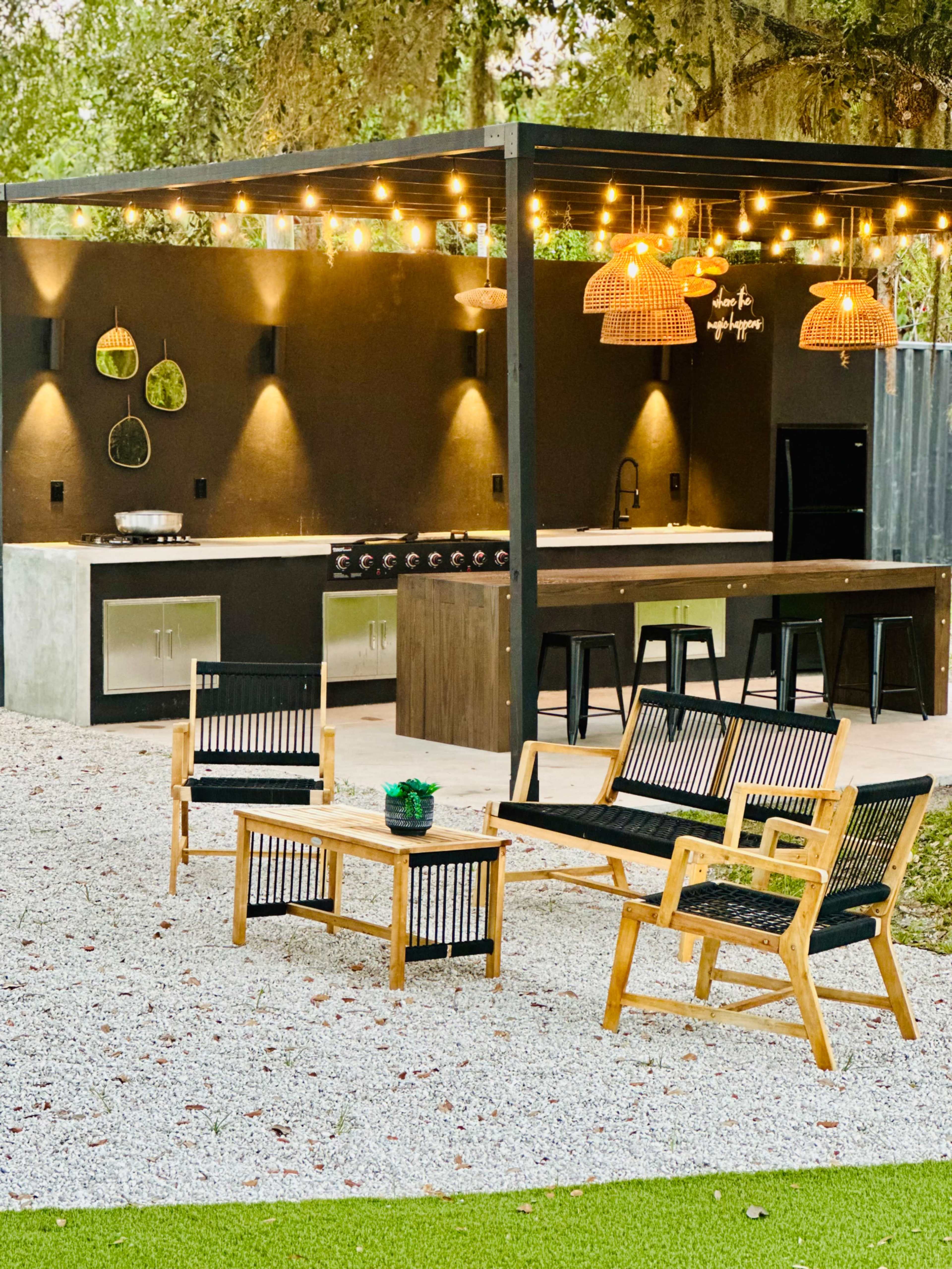The outdoor kitchen area features a covered space with a cooking station, seating arrangements, and decorative lighting.