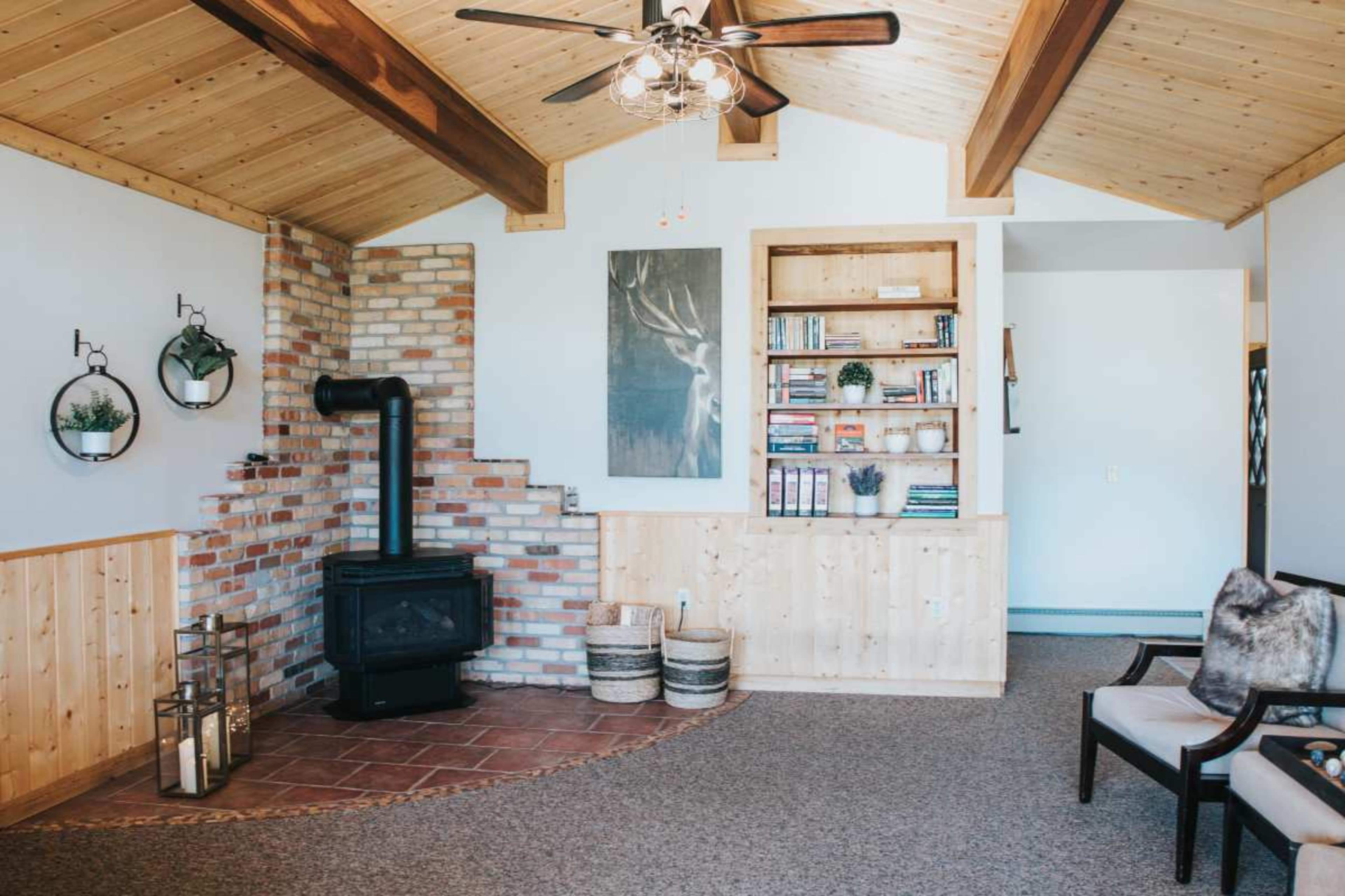 The image shows a spacious living room with a wooden ceiling, a brick fireplace, built-in bookshelves, and a seating area.