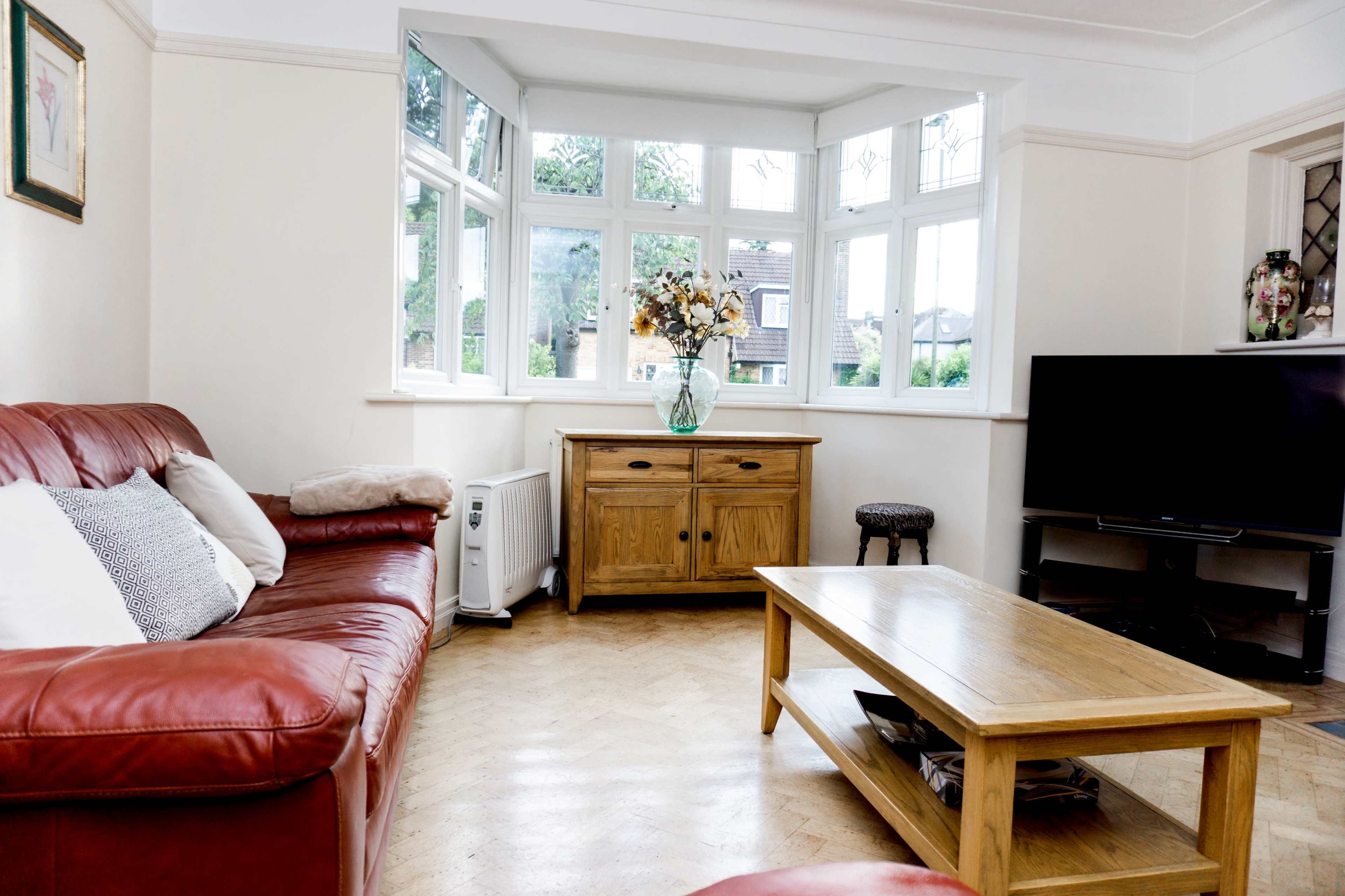 A living room with a red leather sofa, a wooden coffee table, a television, and a console cabinet near a large window adorned with plants and flowers.