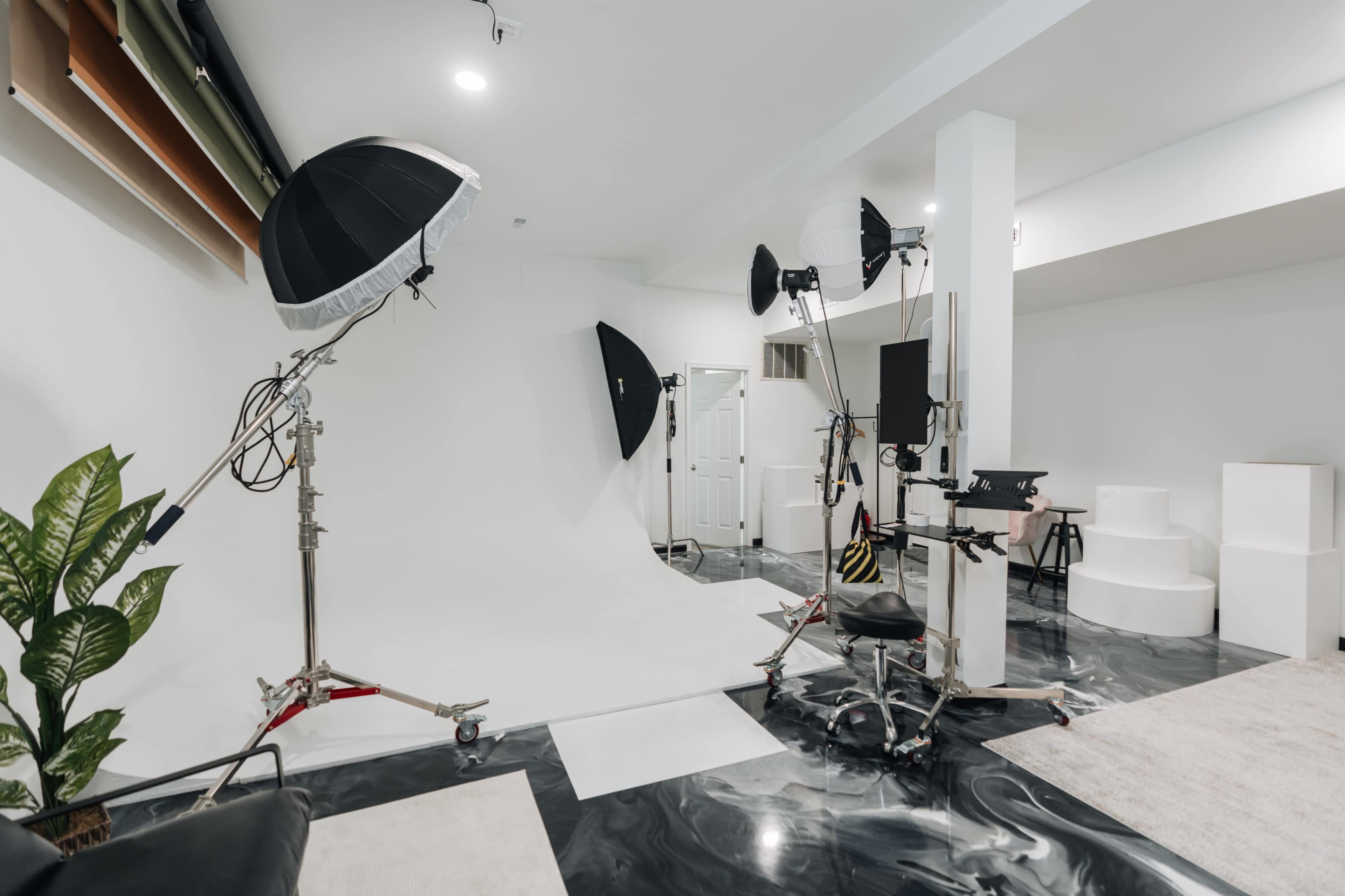 The image shows a photography studio equipped with a white backdrop, various lighting setups, and props scattered around a polished floor.