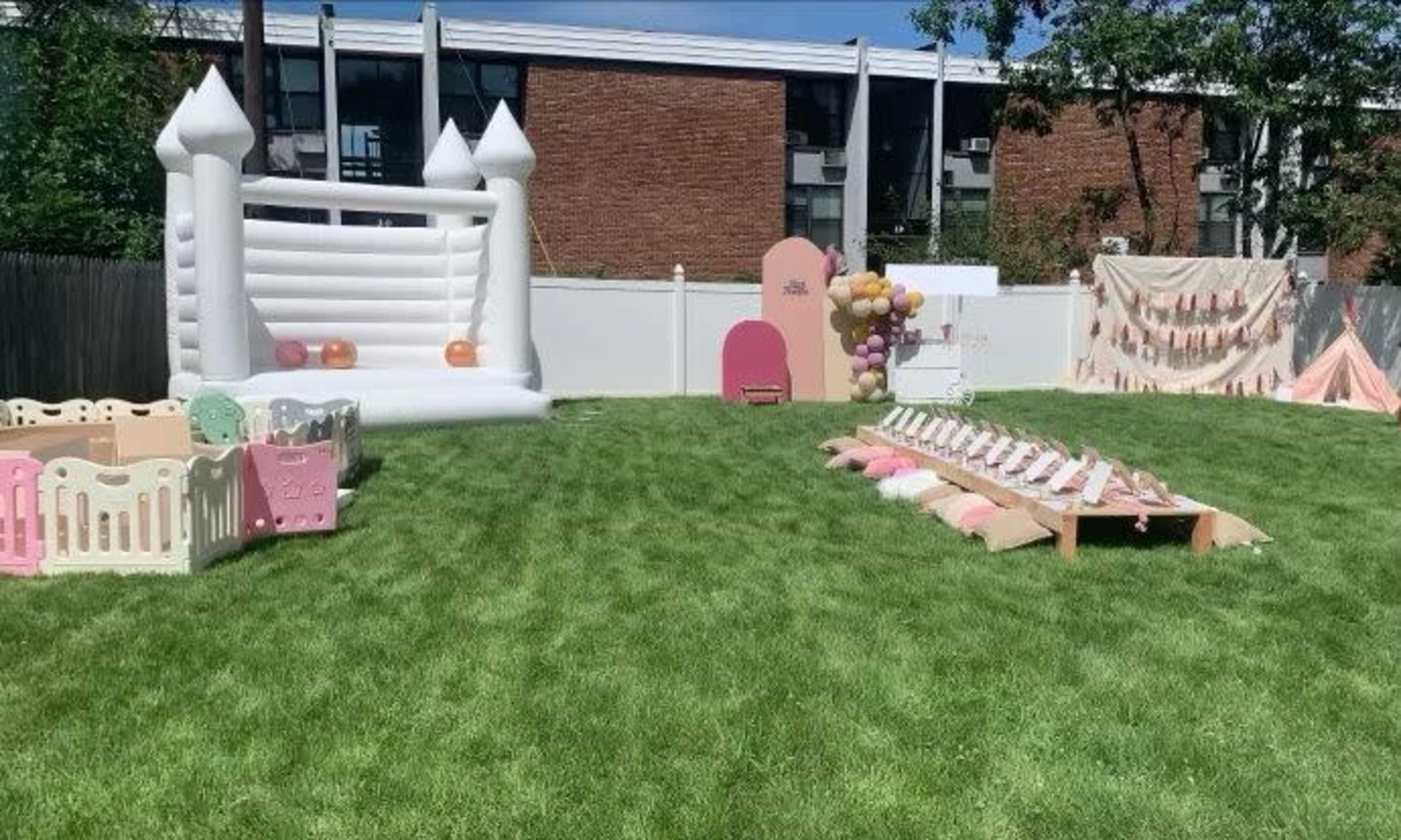 The scene features a backyard party area with a inflatable bounce house, colorful playpen structures, and a decorated space for seating and activities.