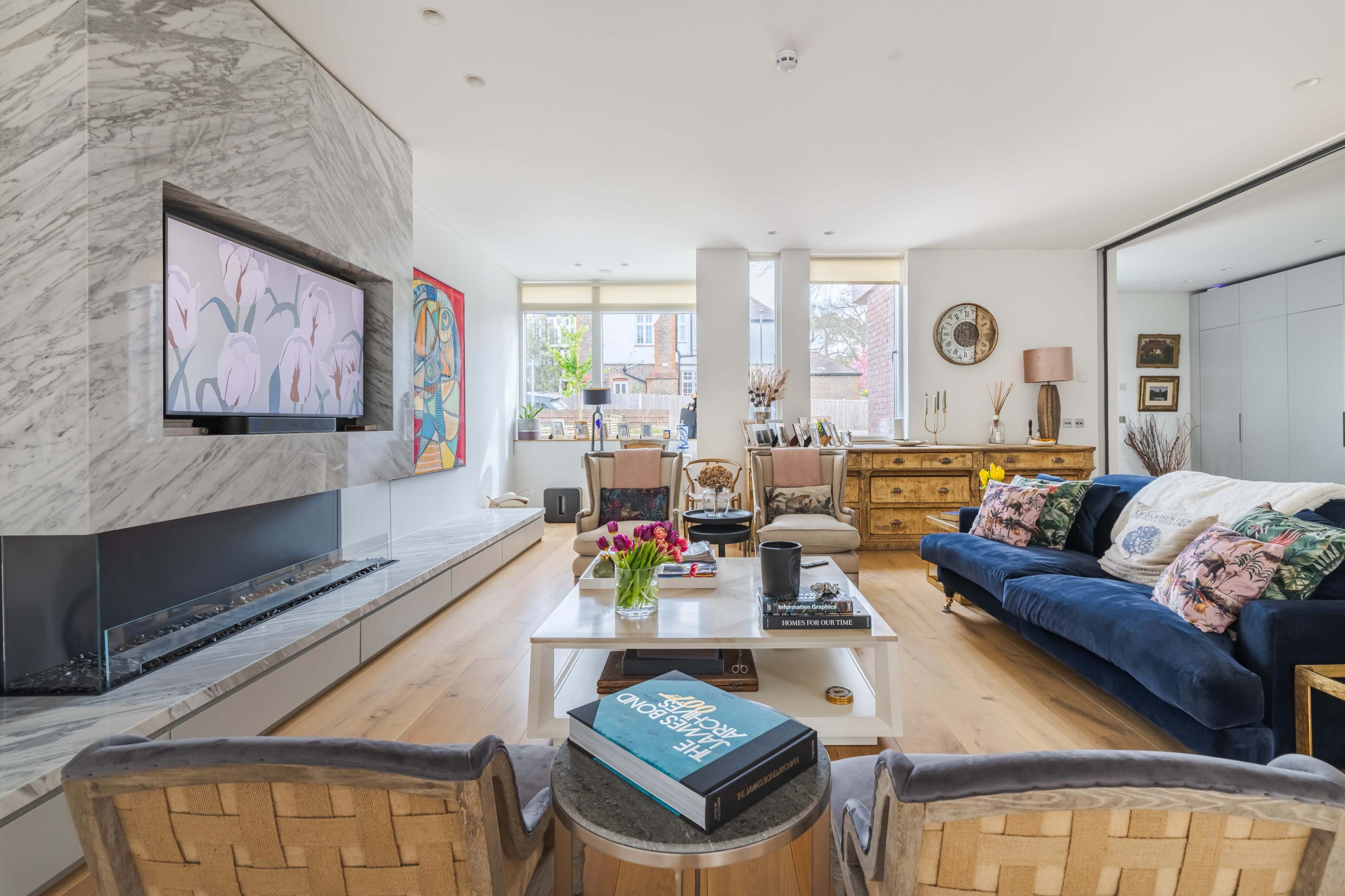 The living room features a marble fireplace, a blue sofa adorned with patterned pillows, and a coffee table topped with books and flowers.