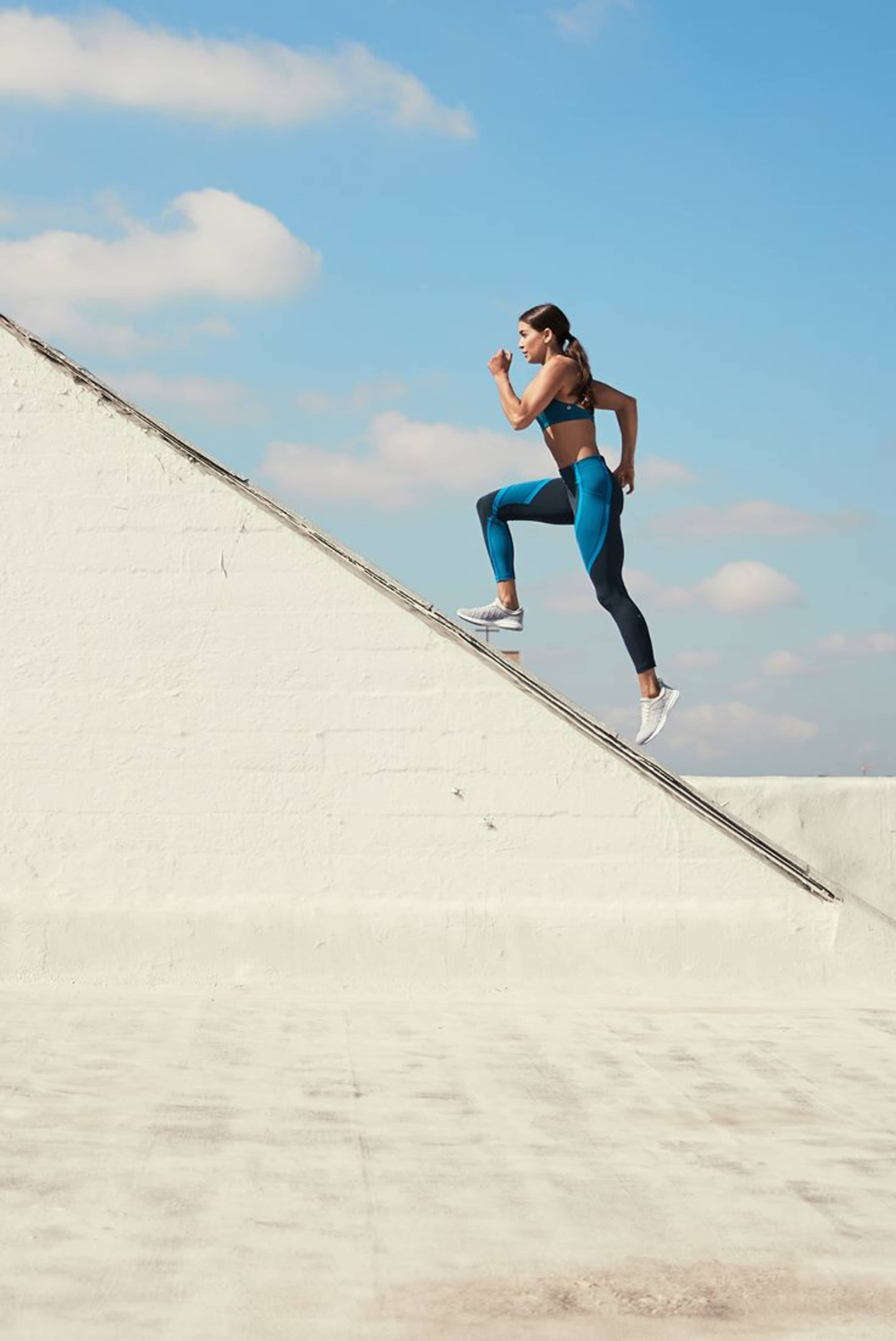A woman in athletic wear runs up an inclined rooftop against a clear blue sky.