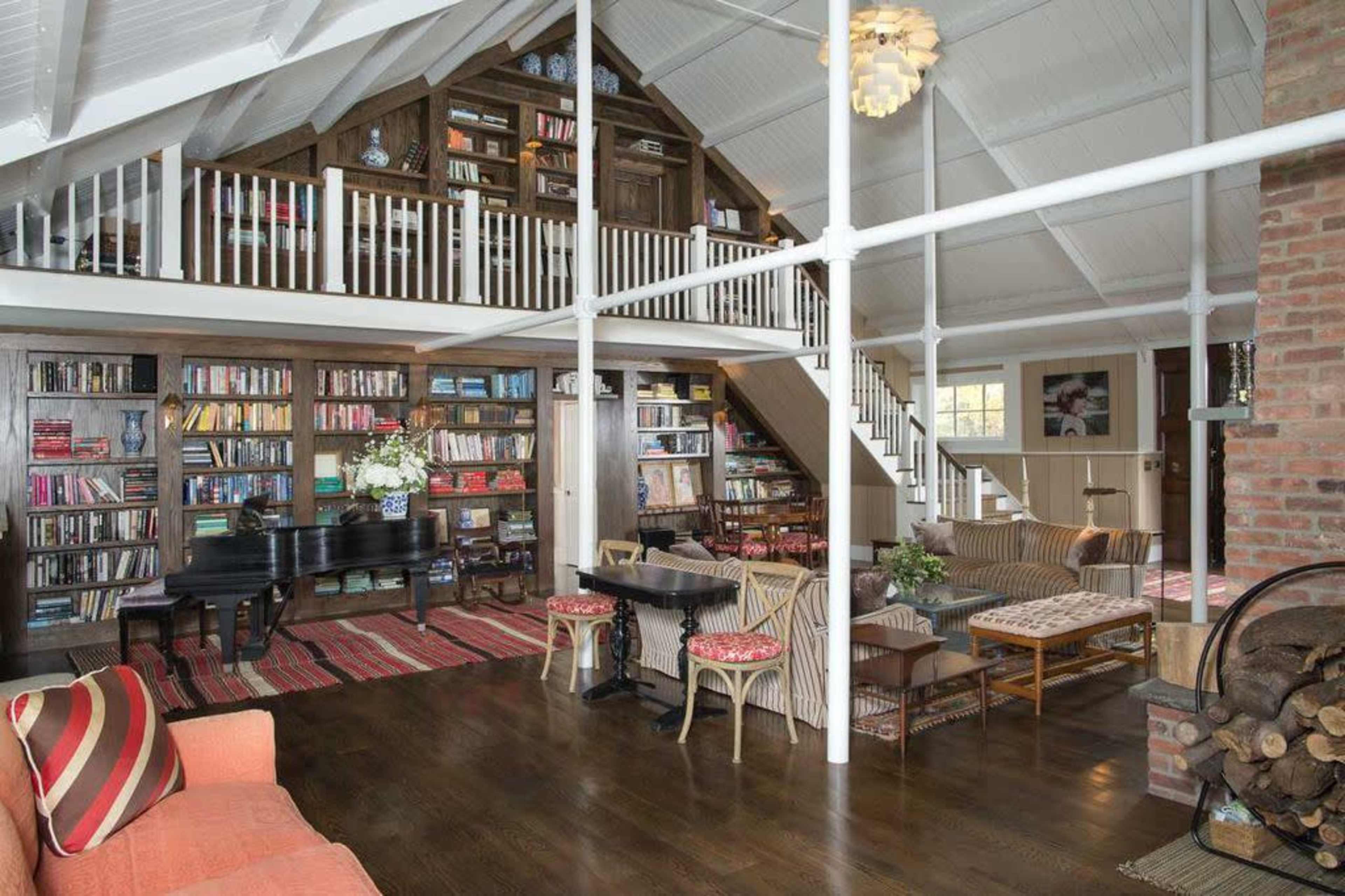 The image shows a spacious living area with a piano, a large bookshelf filled with books, and a comfortable seating arrangement near a fireplace.