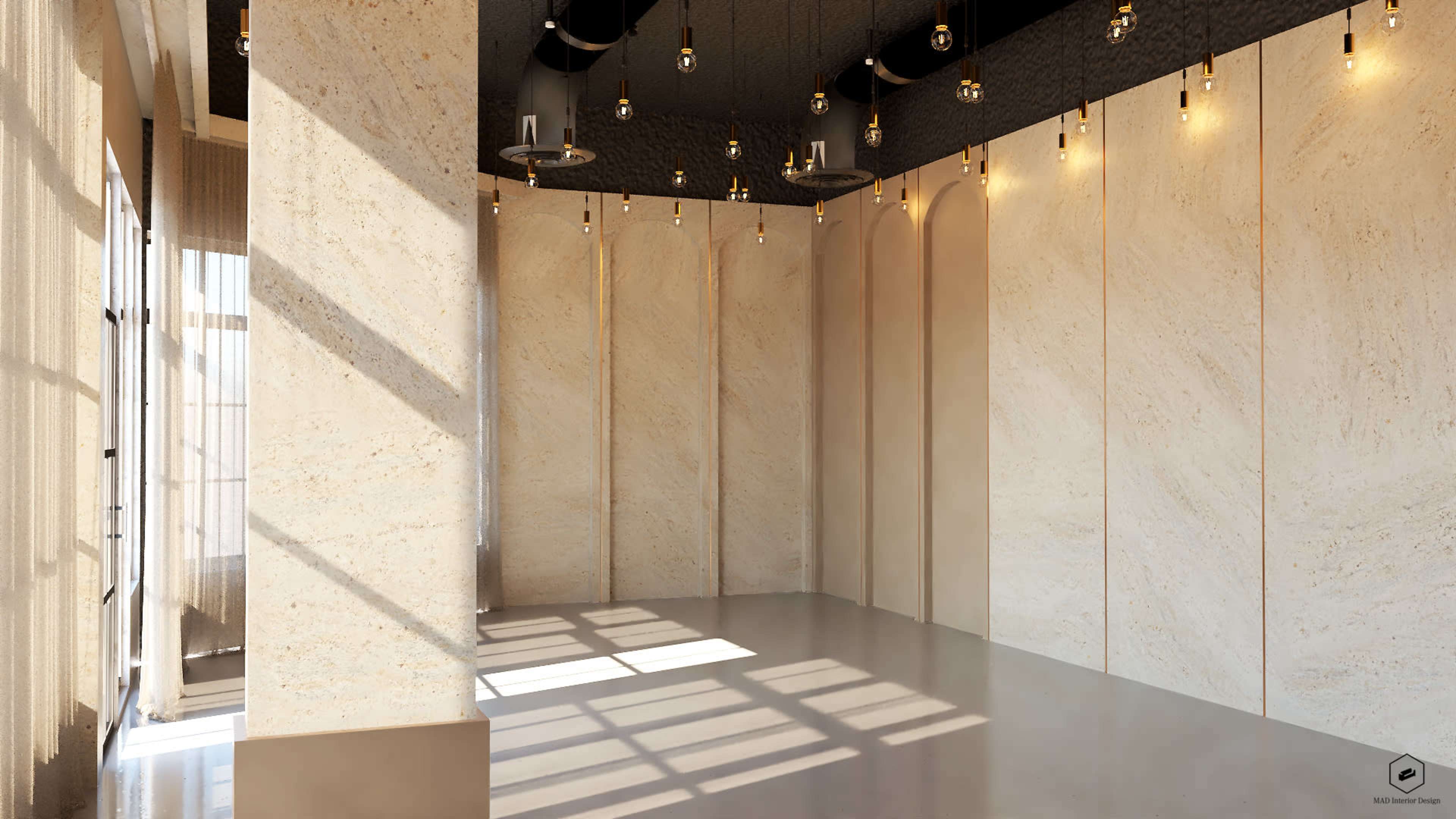 The image shows a spacious, modern room with light-colored stone walls and large windows allowing natural light to enter, along with decorative pendant lights hanging from the ceiling.