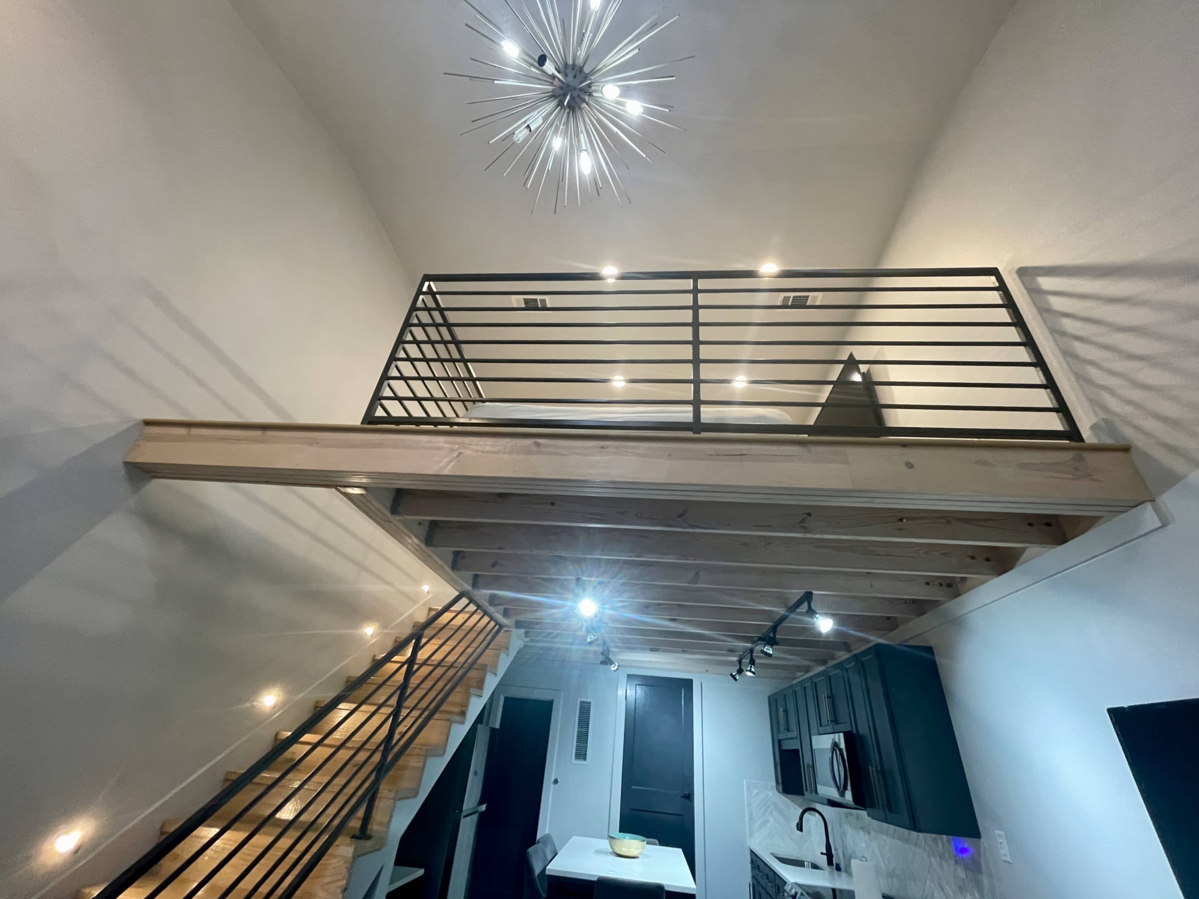 A modern interior space with a lofted sleeping area, wooden beams, and a spiral staircase leading down to a kitchen below.