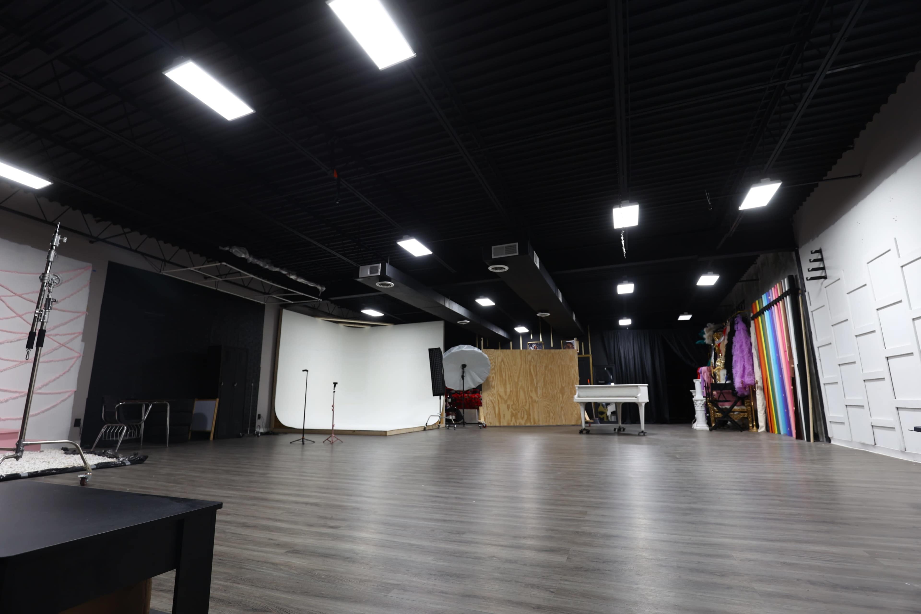 The image shows a spacious indoor studio with a wooden floor, equipped with lighting fixtures, a backdrop area with colorful drapes, and various furniture pieces scattered throughout.