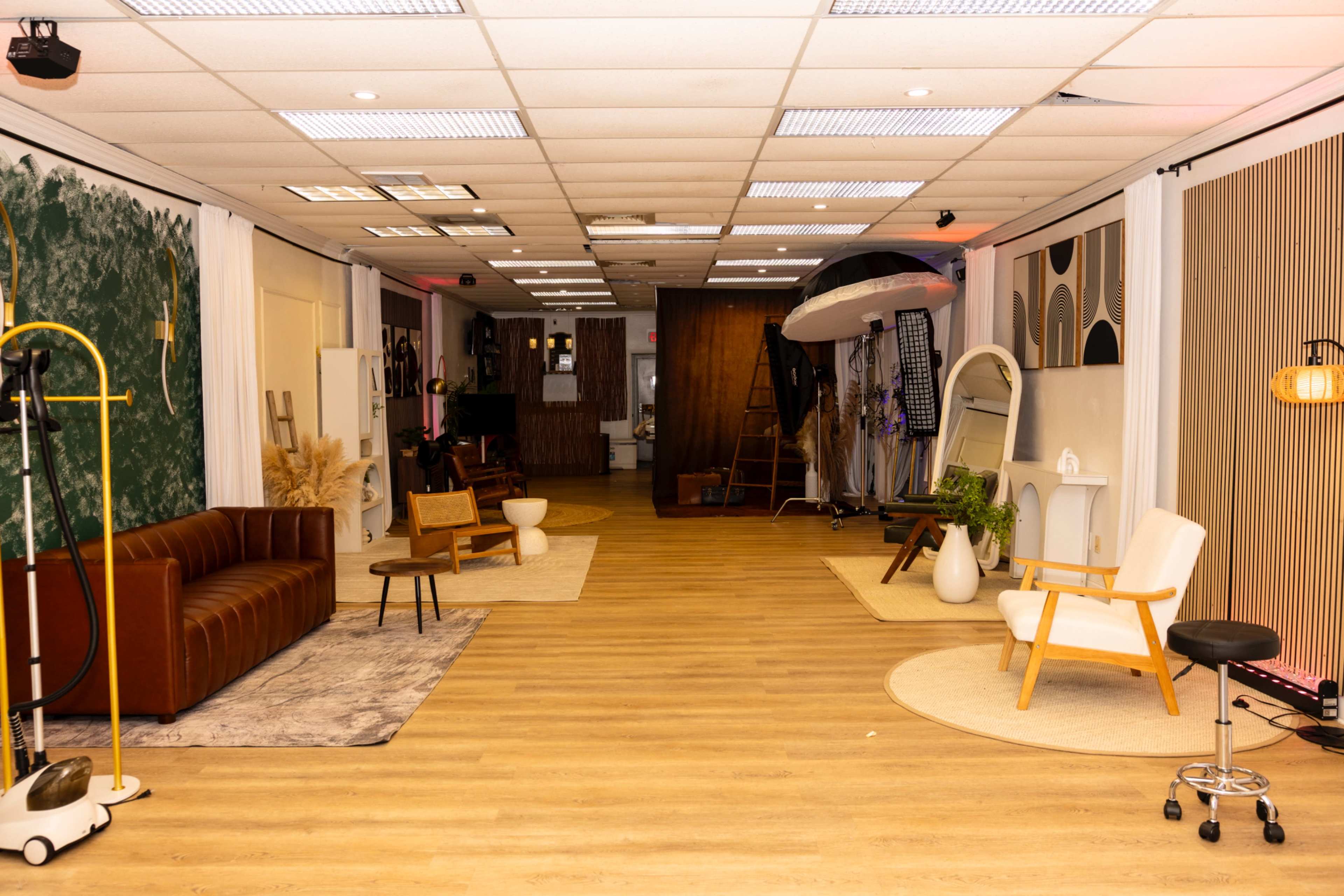 The image shows a spacious interior setup featuring a variety of furniture pieces, including a brown leather sofa, wooden chairs, and decorative elements arranged along a well-lit corridor.