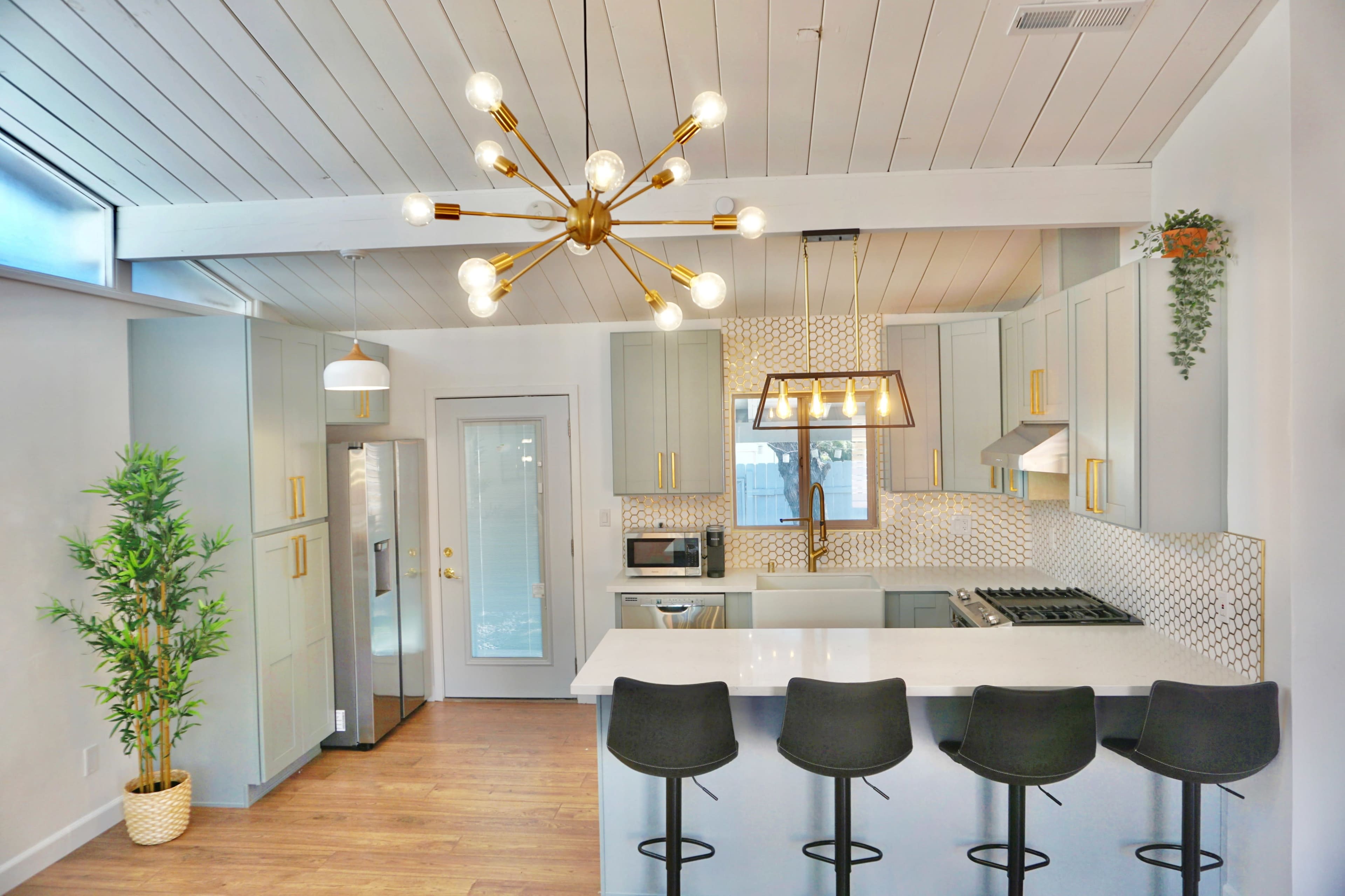 A modern kitchen with light-colored cabinets, a large island with bar stools, and a distinctive chandelier.