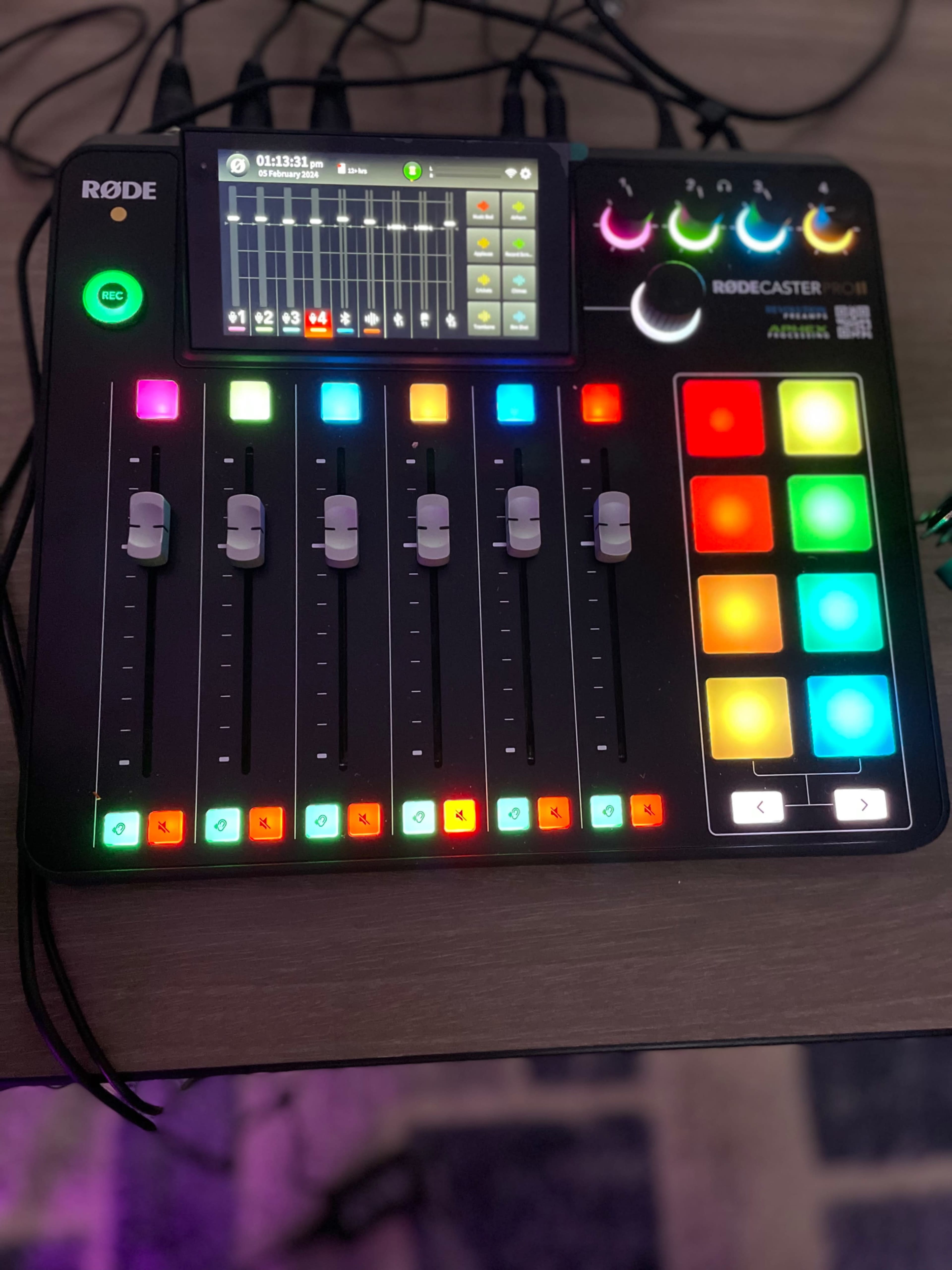 A Rodecaster Pro audio interface with multiple sliders, buttons, and a touchscreen display illuminated in various colors.