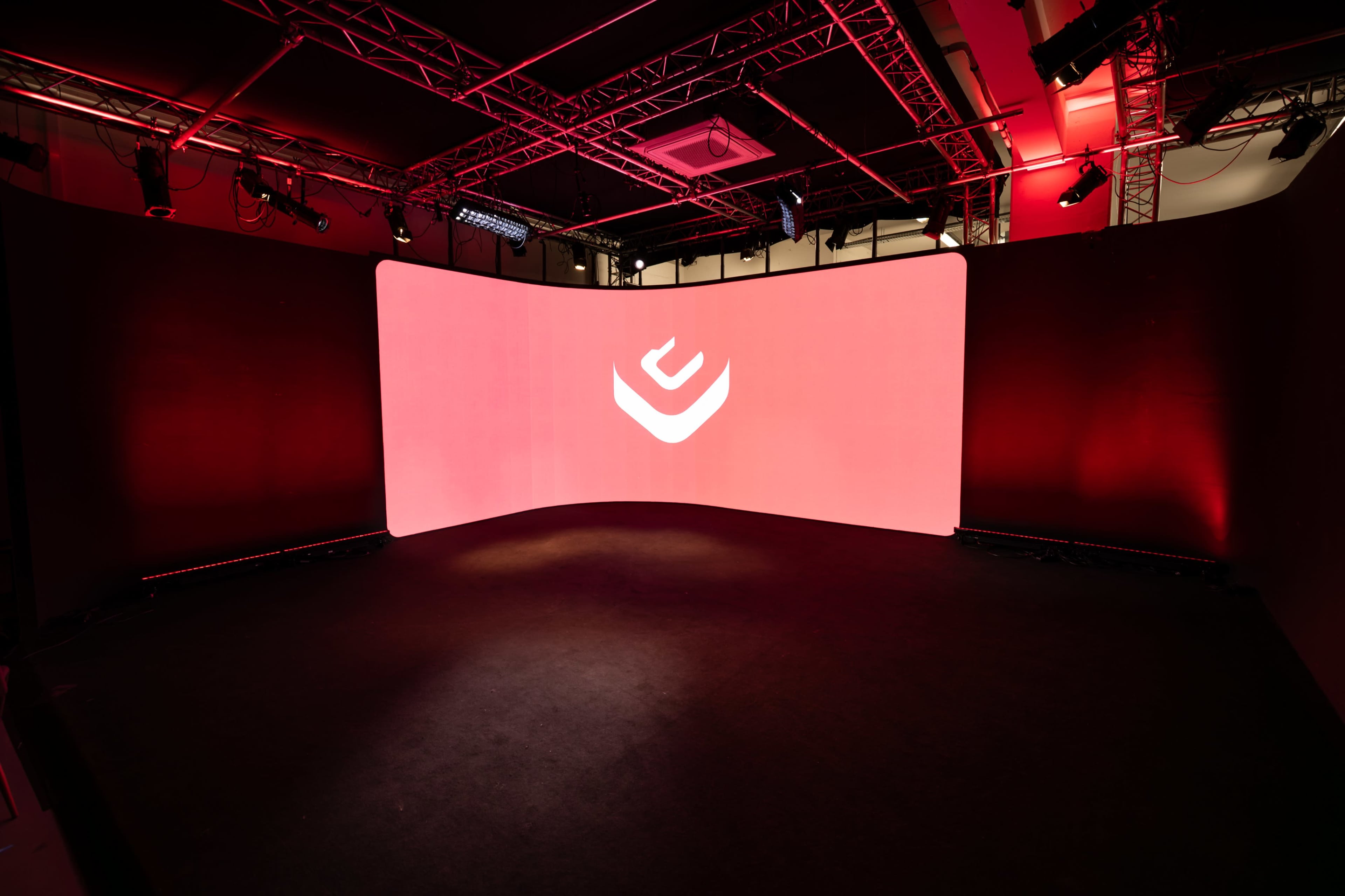 A sleek stage setup with a large curved screen illuminated in red, featuring a central logo.