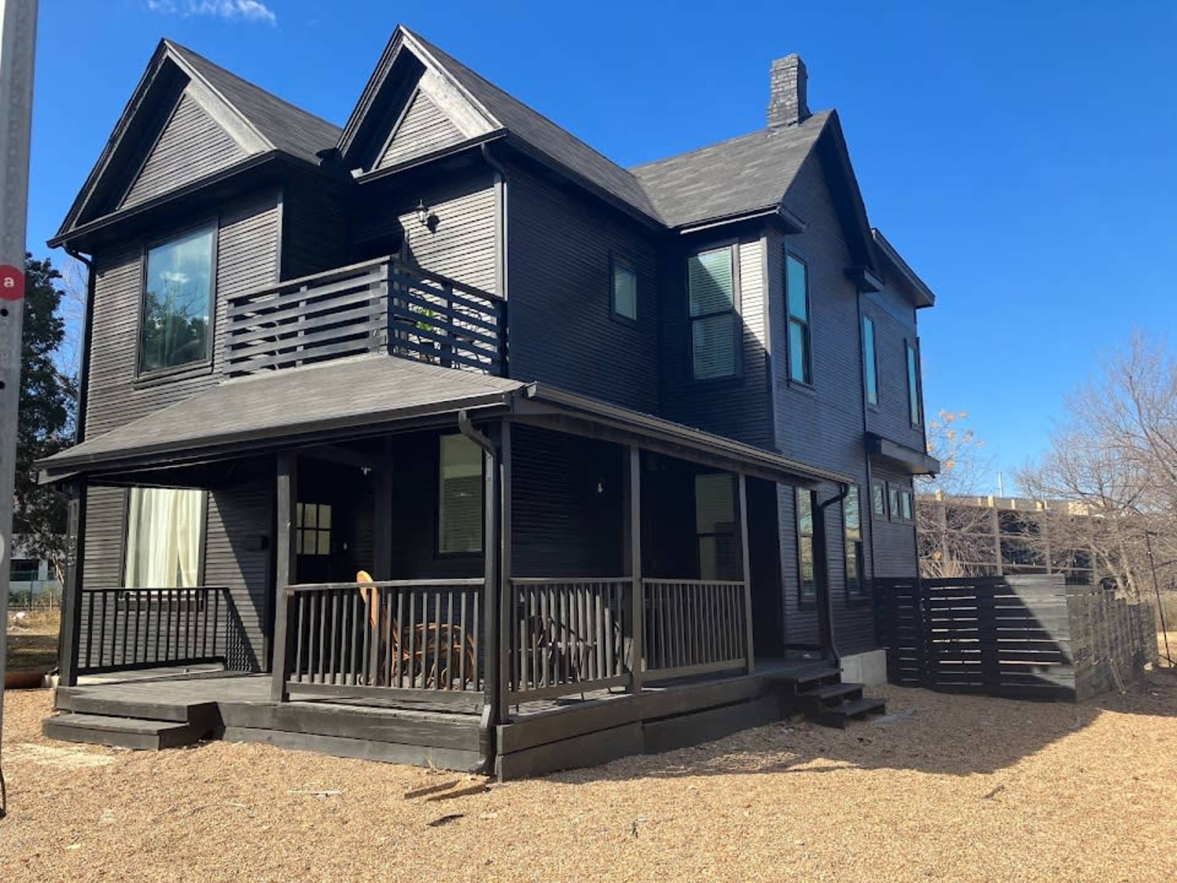 A black-painted two-story house features a porch with a railing and a landscaped gravel yard.
