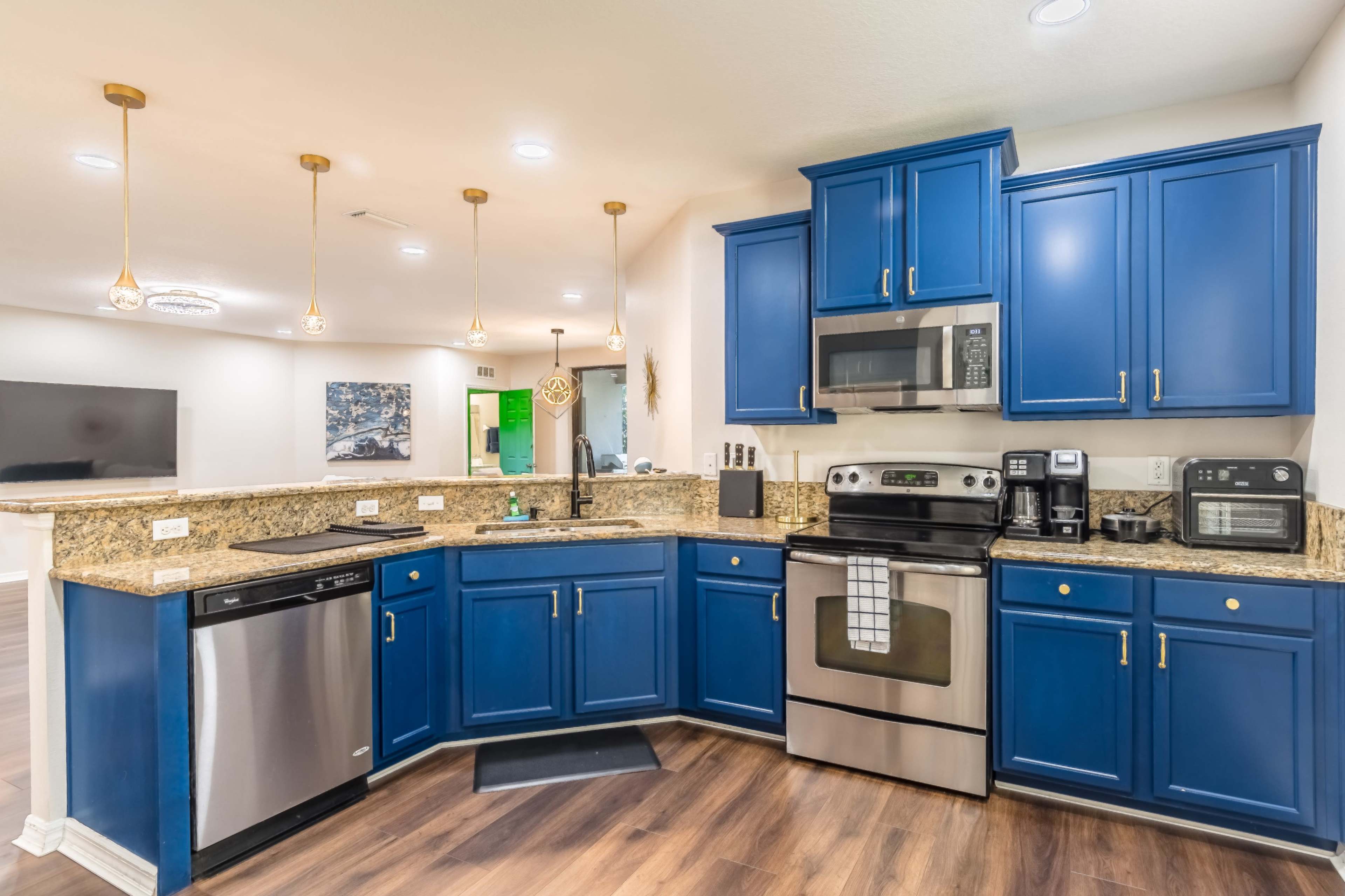 A modern kitchen featuring blue cabinets, granite countertops, stainless steel appliances, and pendant lighting.