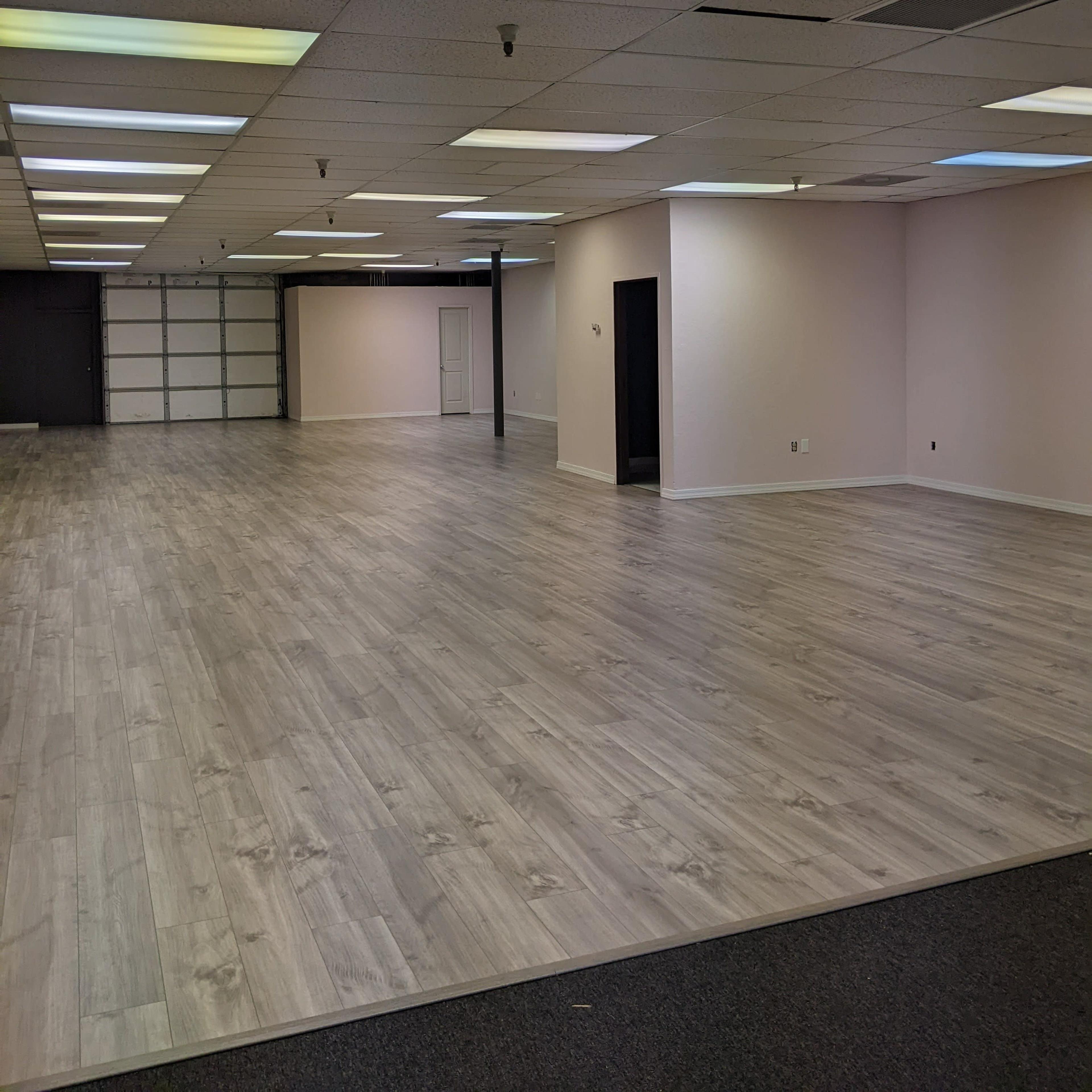 A large, empty interior space with light-colored wood flooring and gray walls.