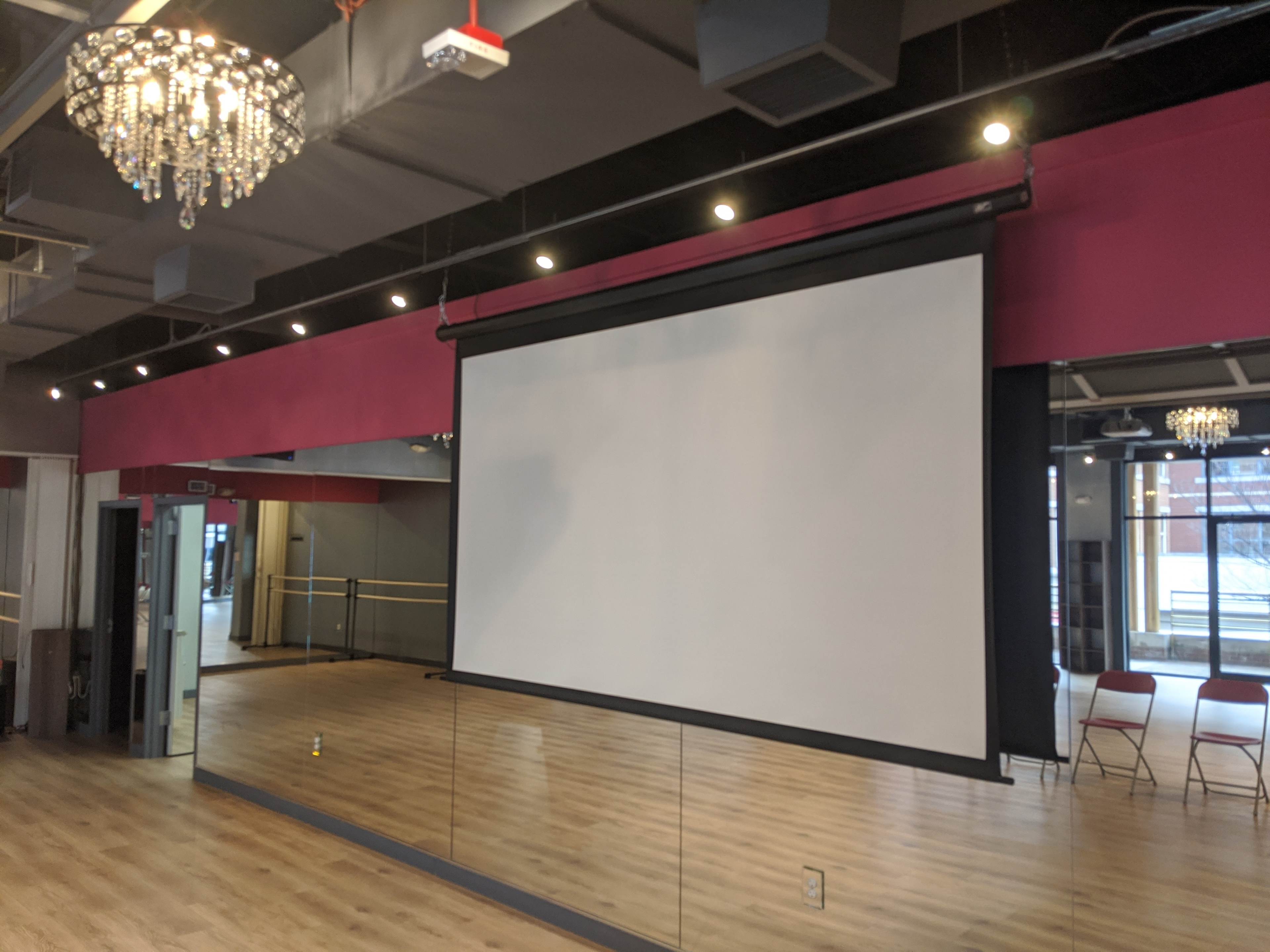 A dance studio with a mirrored wall, a projector screen, and crystal chandeliers hanging from the ceiling.