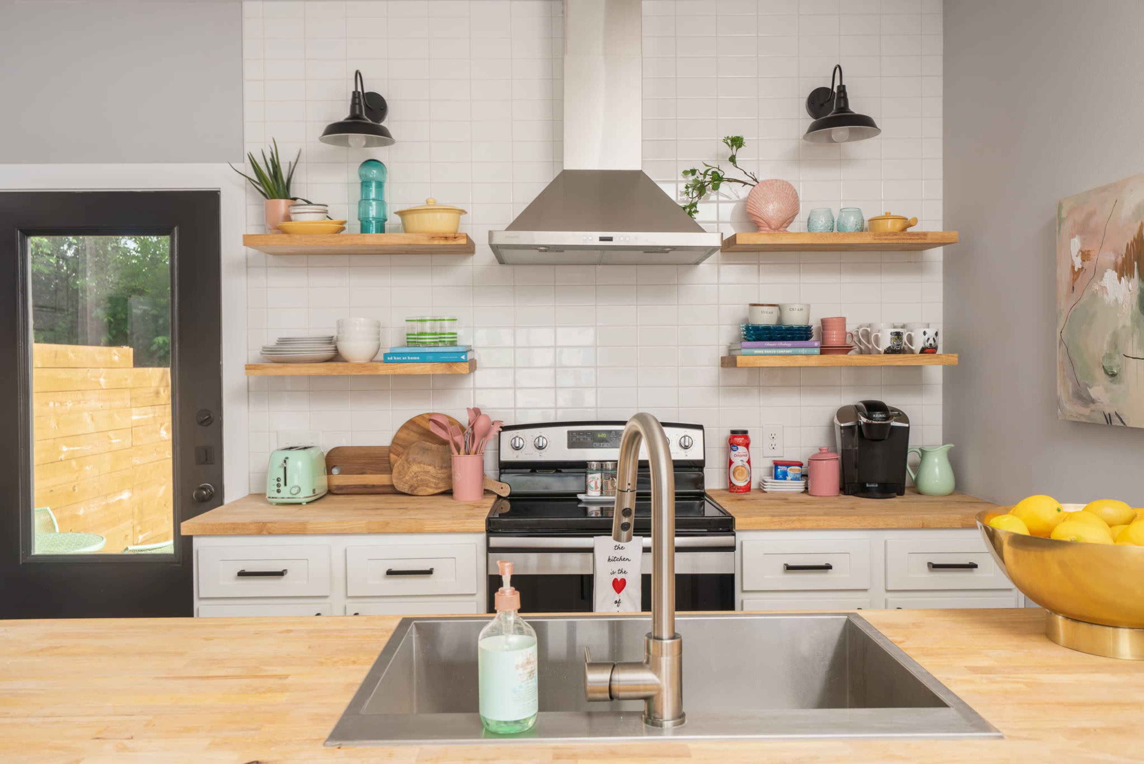 A modern kitchen with a stainless steel stove, open shelving displaying various kitchenware, and a large sink on a wooden countertop.