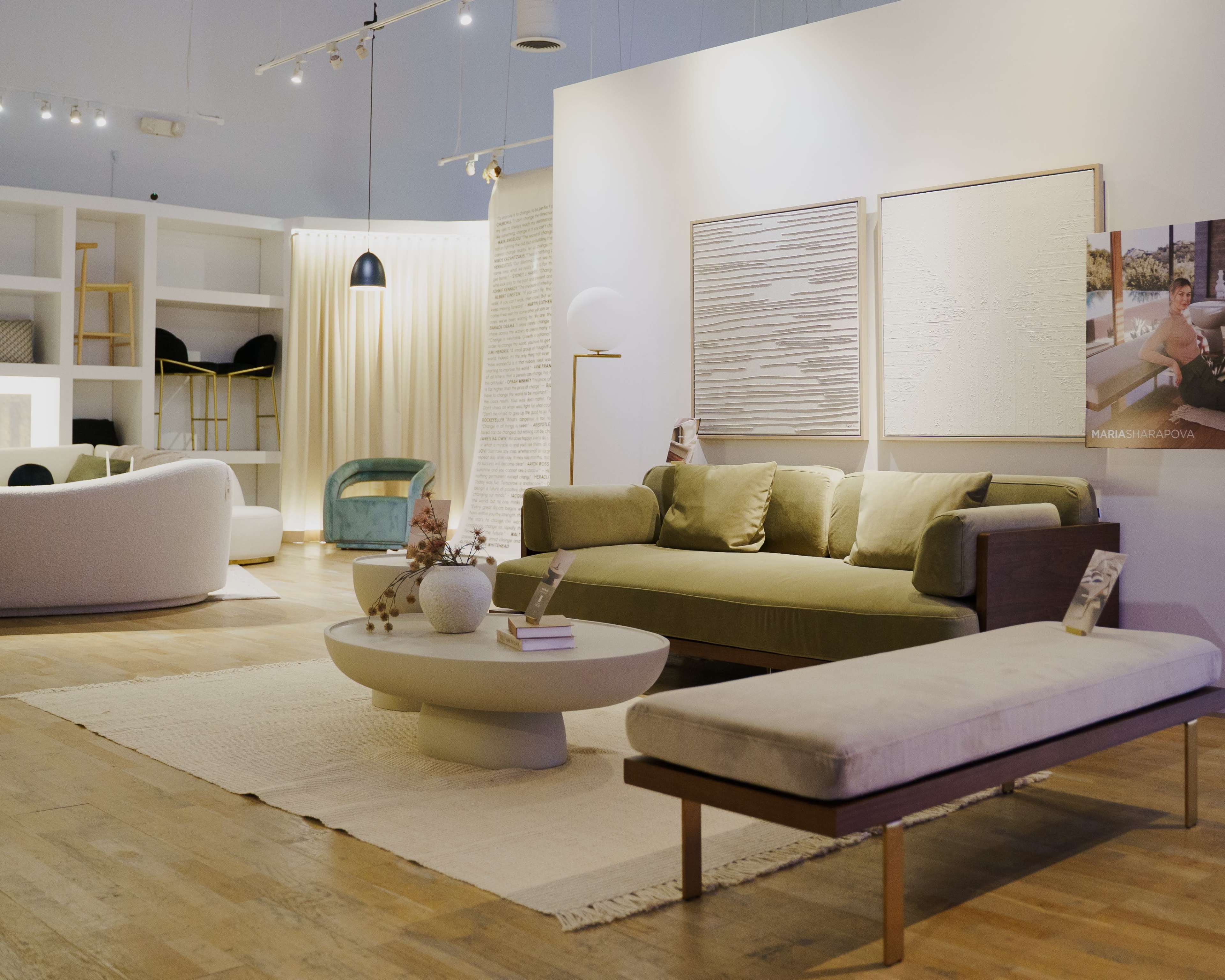A modern living room display features a green sofa, a round coffee table, a long bench, and abstract wall art.