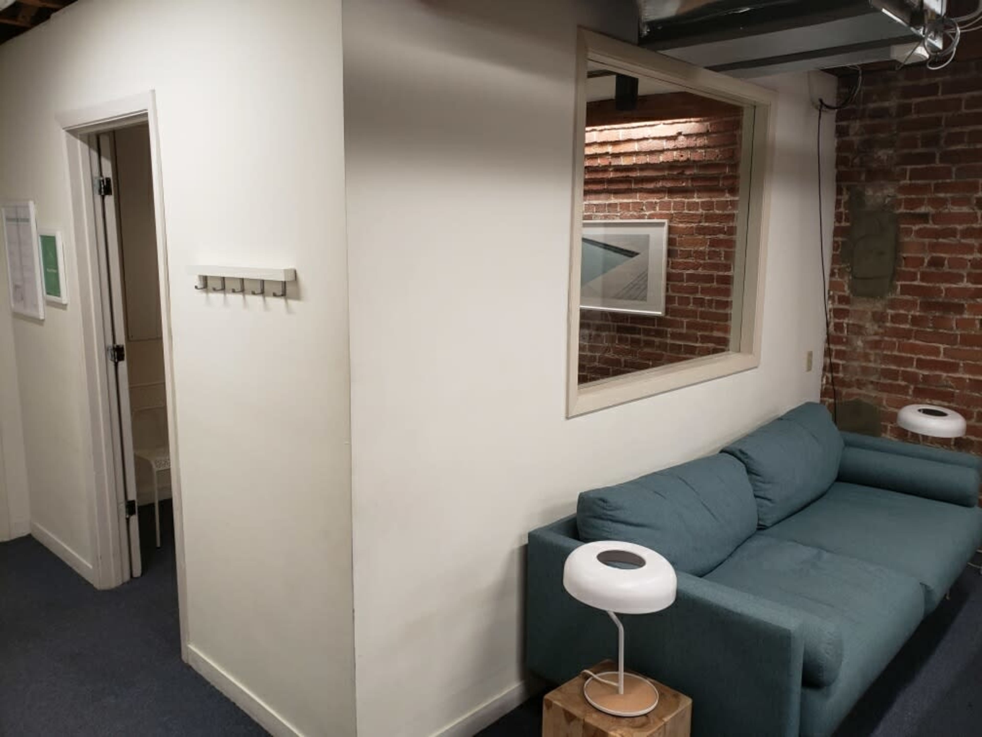 A small room featuring a green couch, a wall with exposed brick, and a door leading to another space in the background.