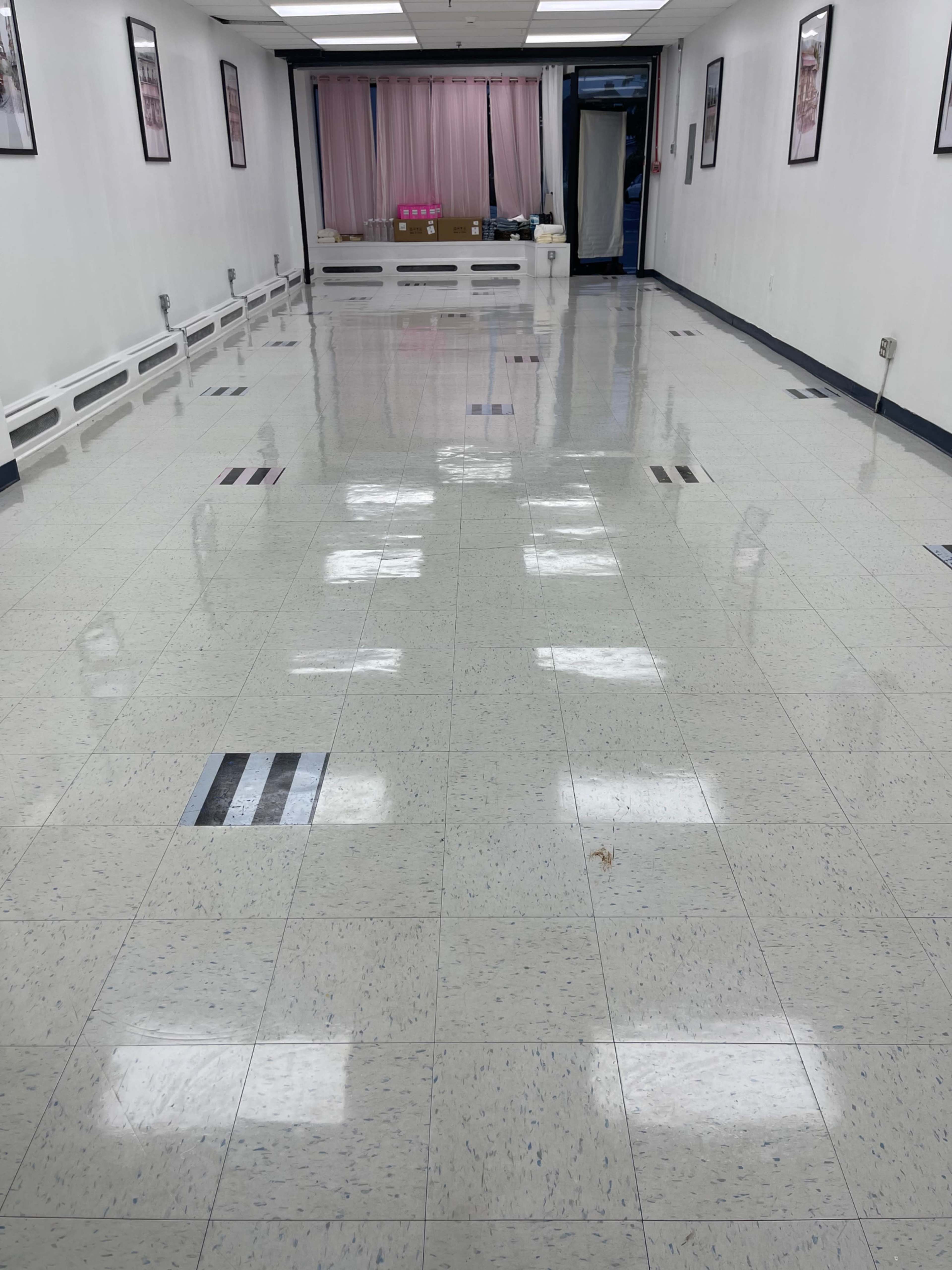 The image shows a clean, well-lit empty room with a glossy tiled floor and framed images on the walls.