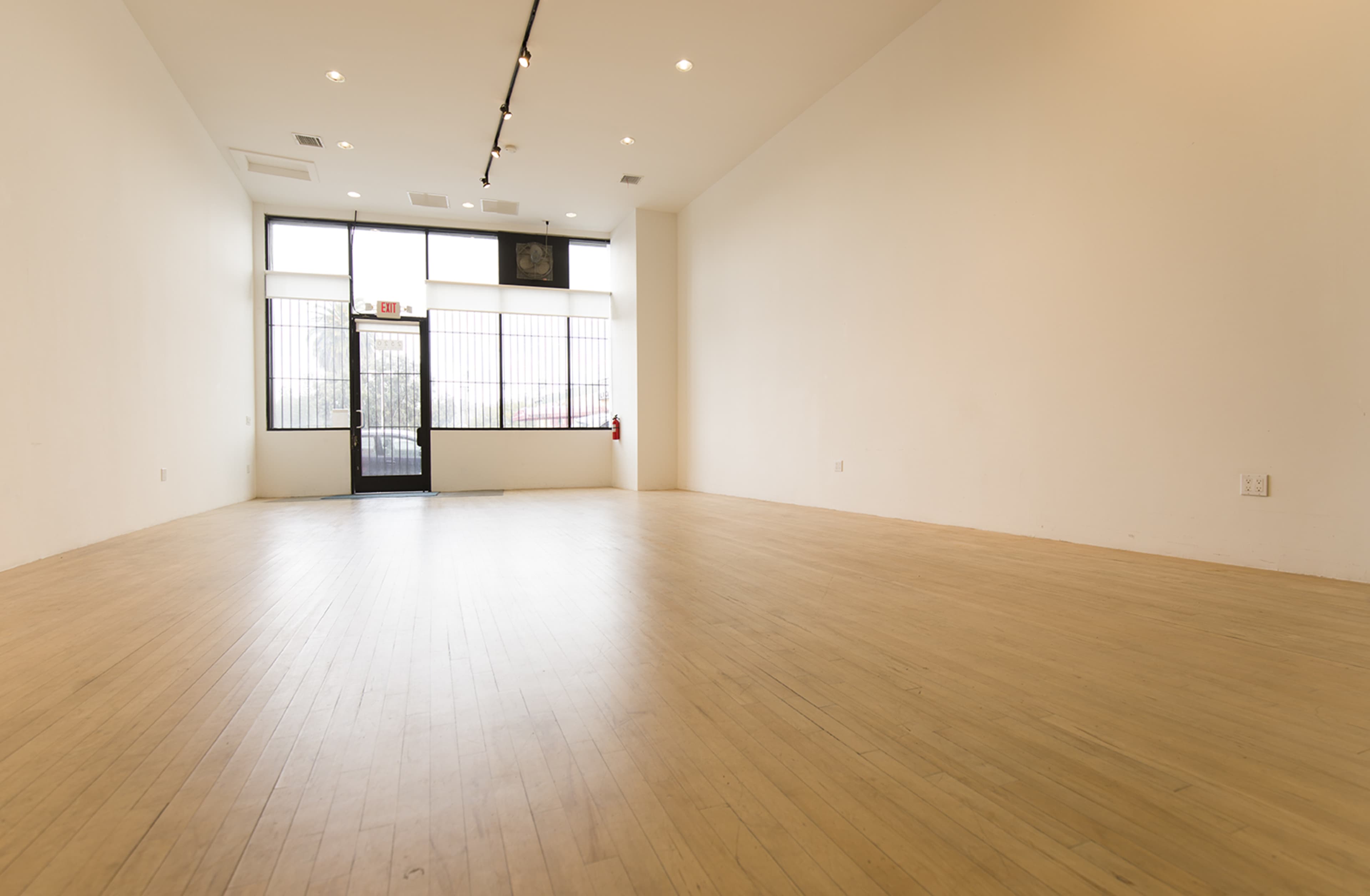The image shows an empty room with wooden flooring and a large window at the entrance.