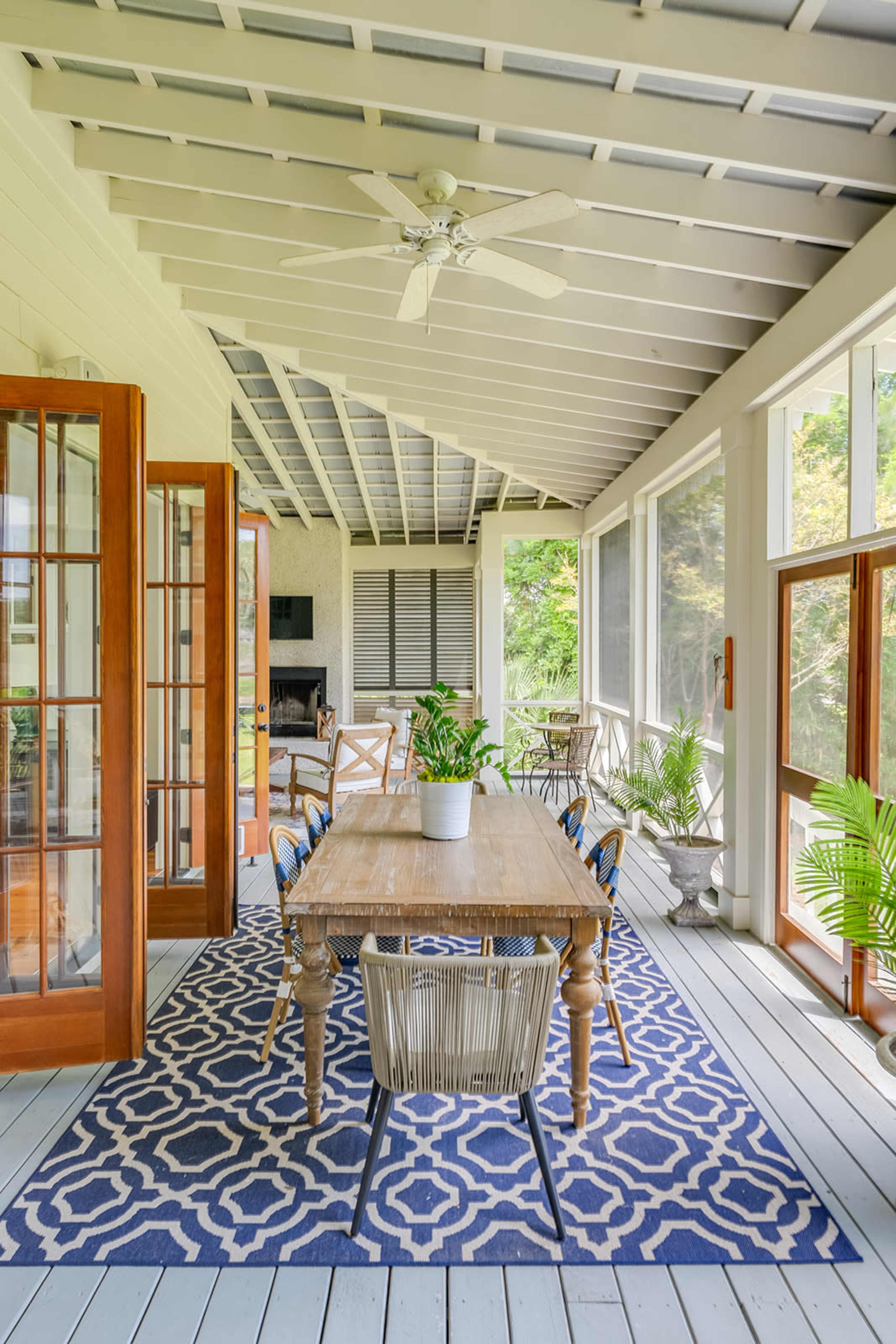 A spacious sunroom features a wooden dining table surrounded by chairs, with large windows letting in natural light and greenery outside.
