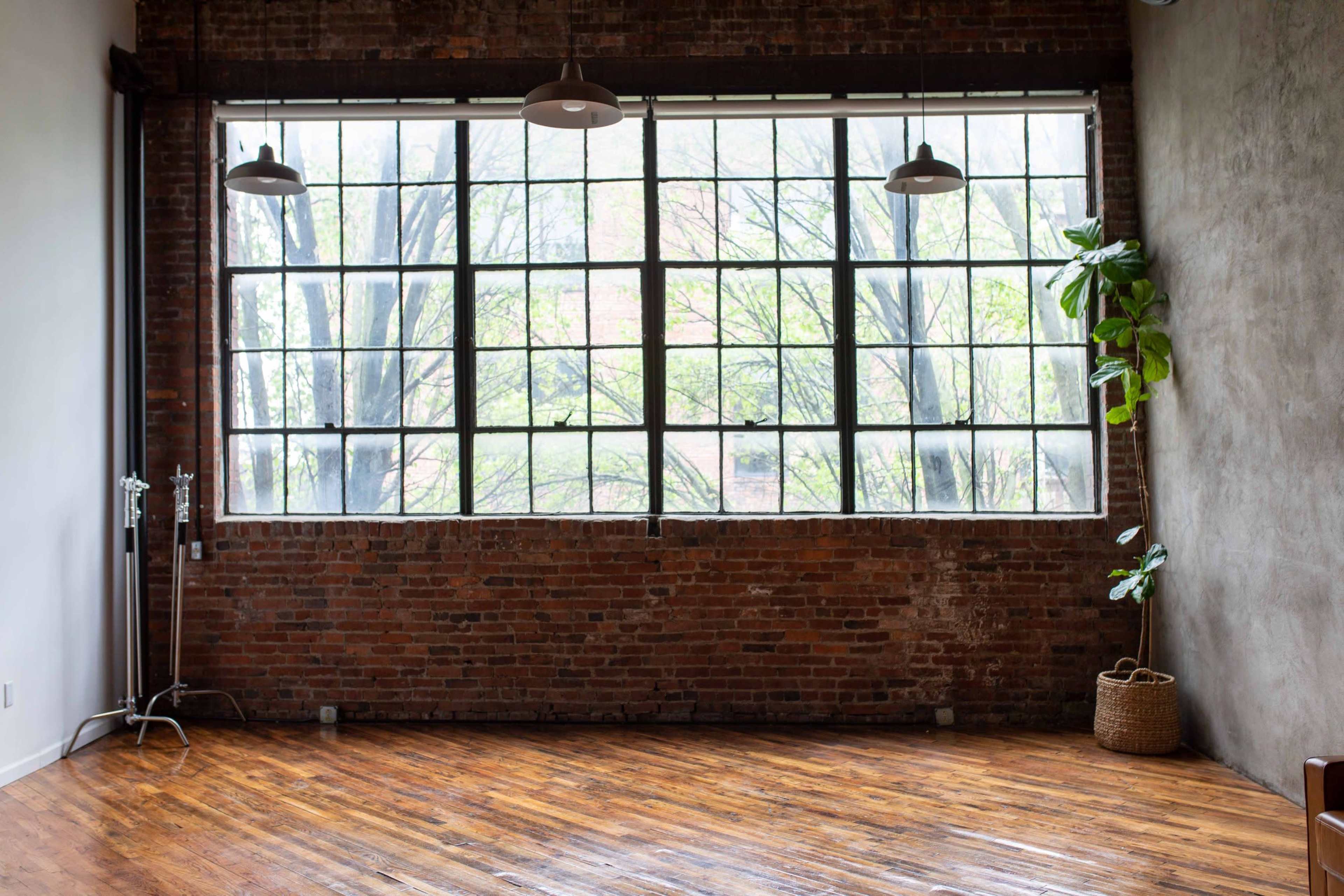 The image features an industrial-style room with a large window, exposed brick walls, and a polished wooden floor.
