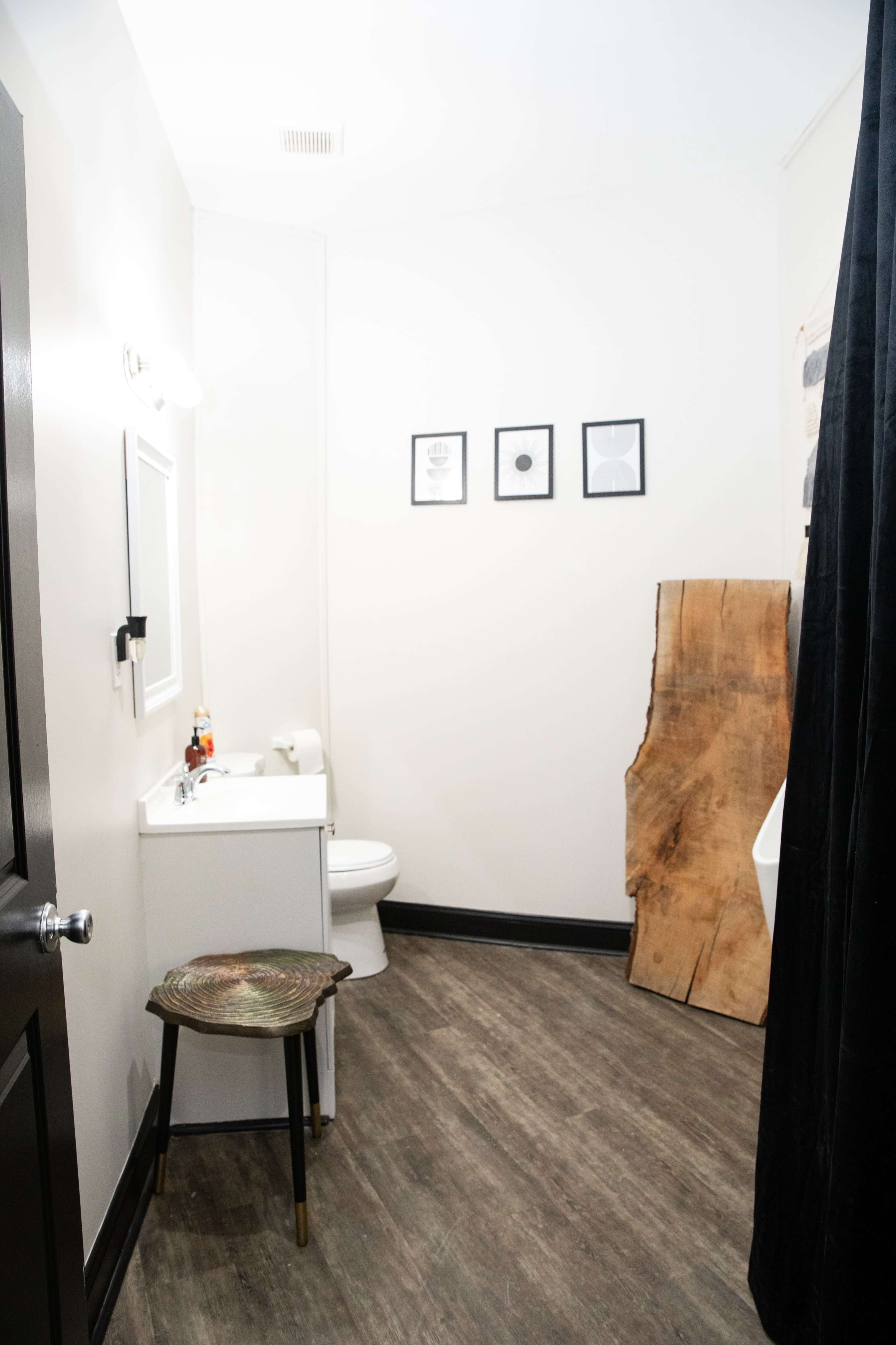 A small bathroom with a toilet, a sink, a framed mirror, four framed pictures on the wall, and a wooden accent piece next to the sink.