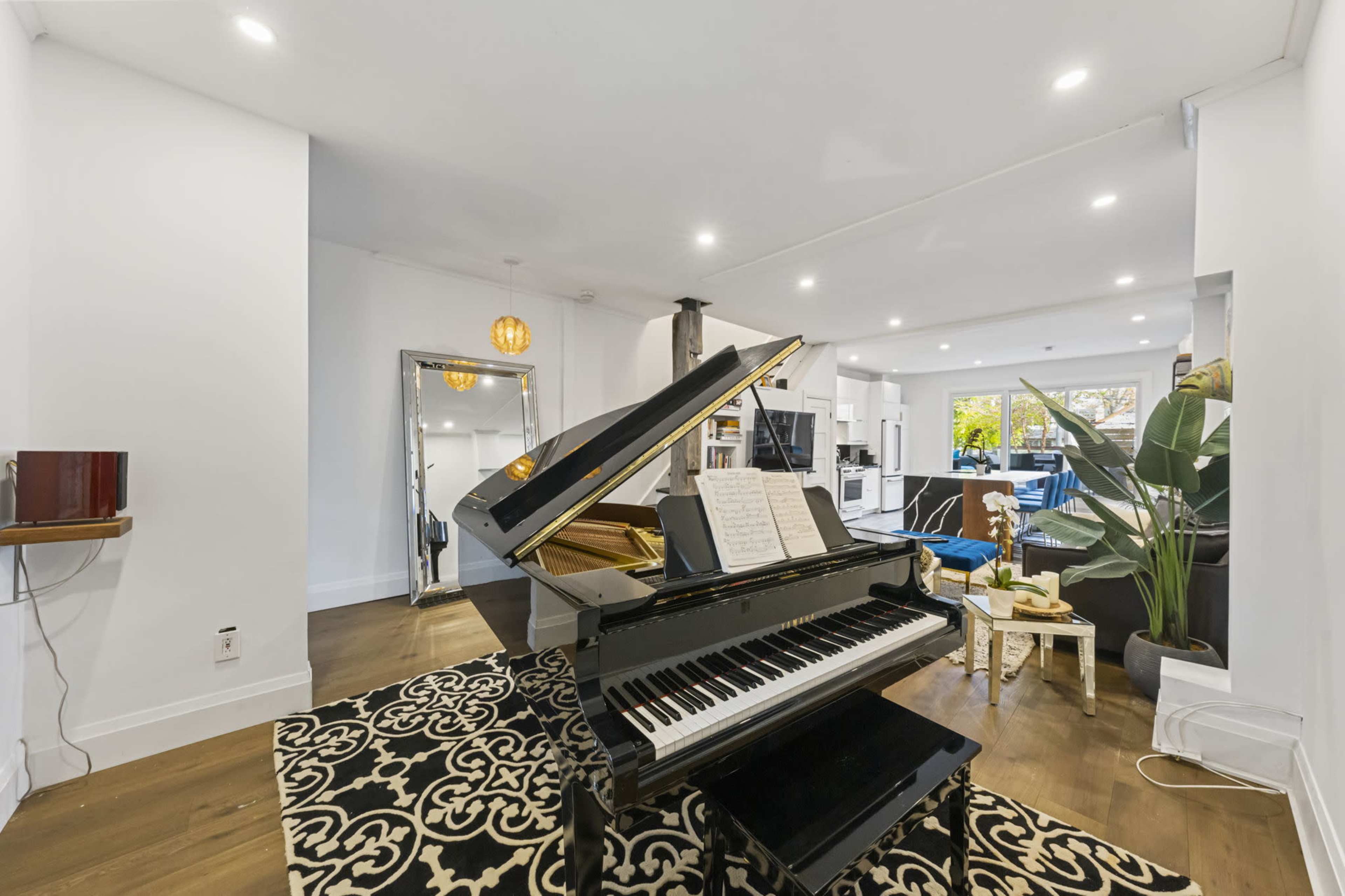 A grand piano sits in the foreground of a bright living room featuring modern furniture and decor.