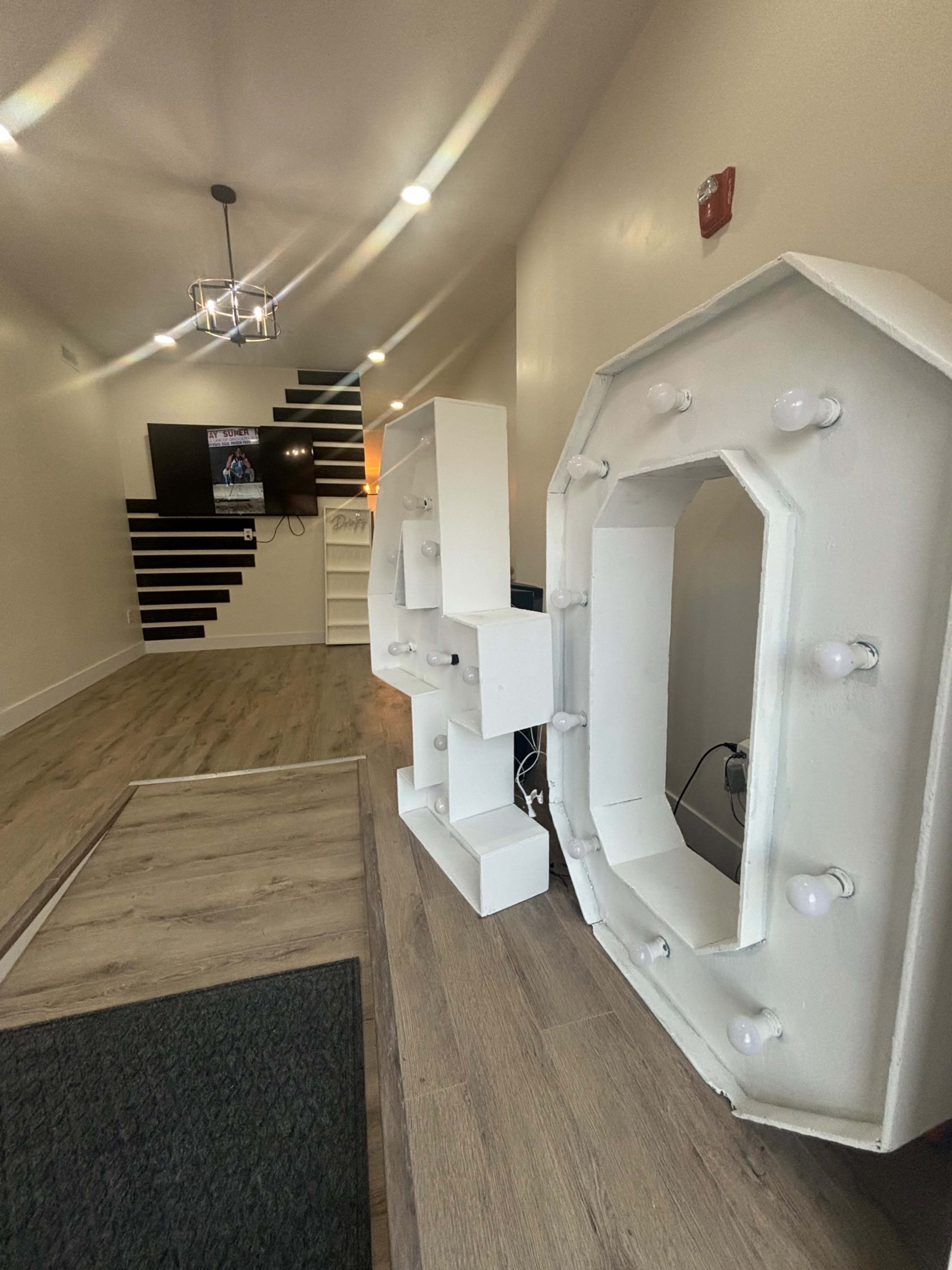 The image shows a modern interior space with a large, illuminated marquee sign reading "40" positioned on the floor, a TV mounted on the wall, and a staircase with black and white detailing.