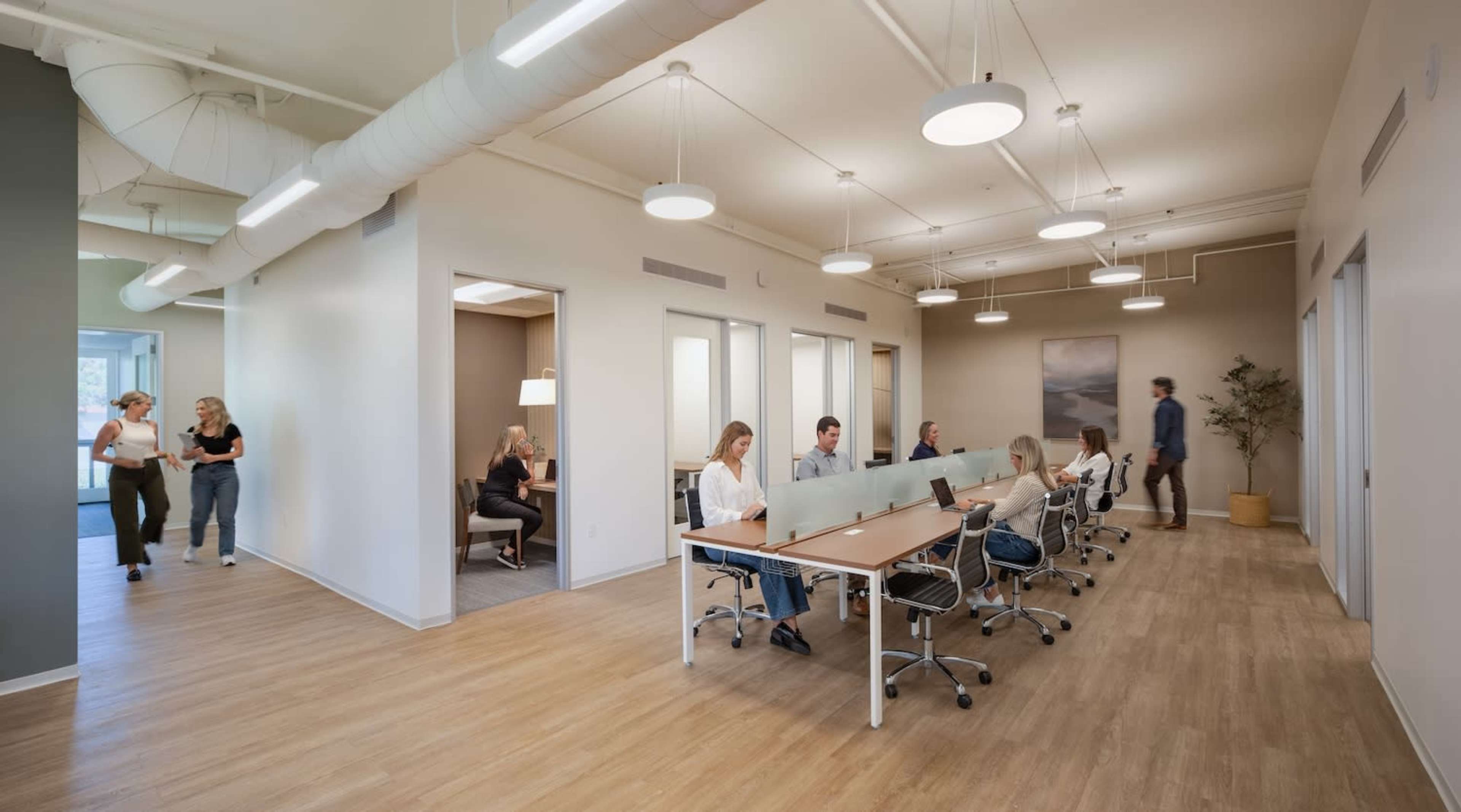 A modern office space with several people working at desks and others walking through the area.
