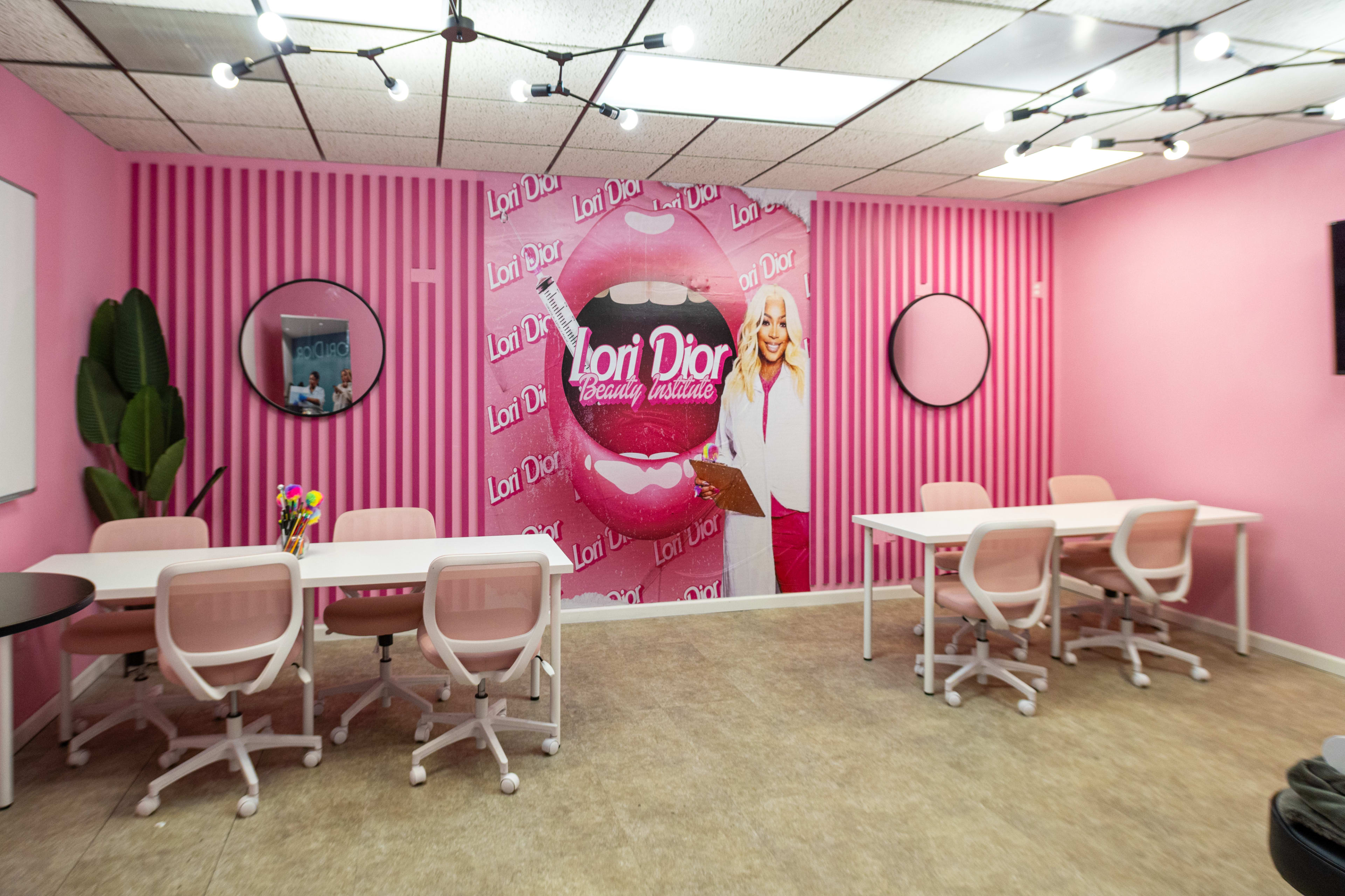 A beauty studio with pink striped walls, featuring a large mural of a mouth with the text "Lori Dior" and two round mirrors, complemented by white tables and chairs.