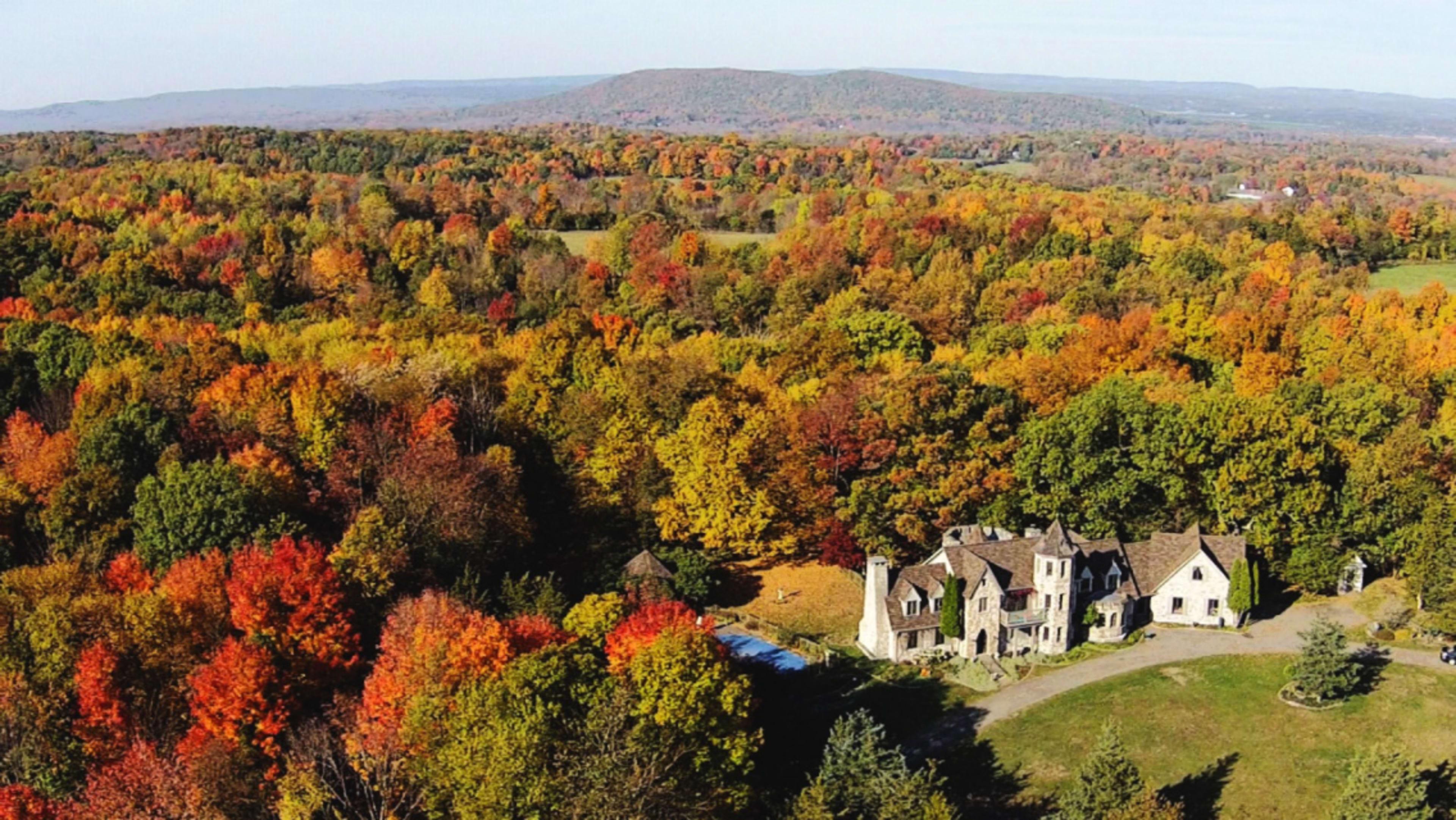A stone mansion surrounded by vibrant fall foliage and rolling hills.