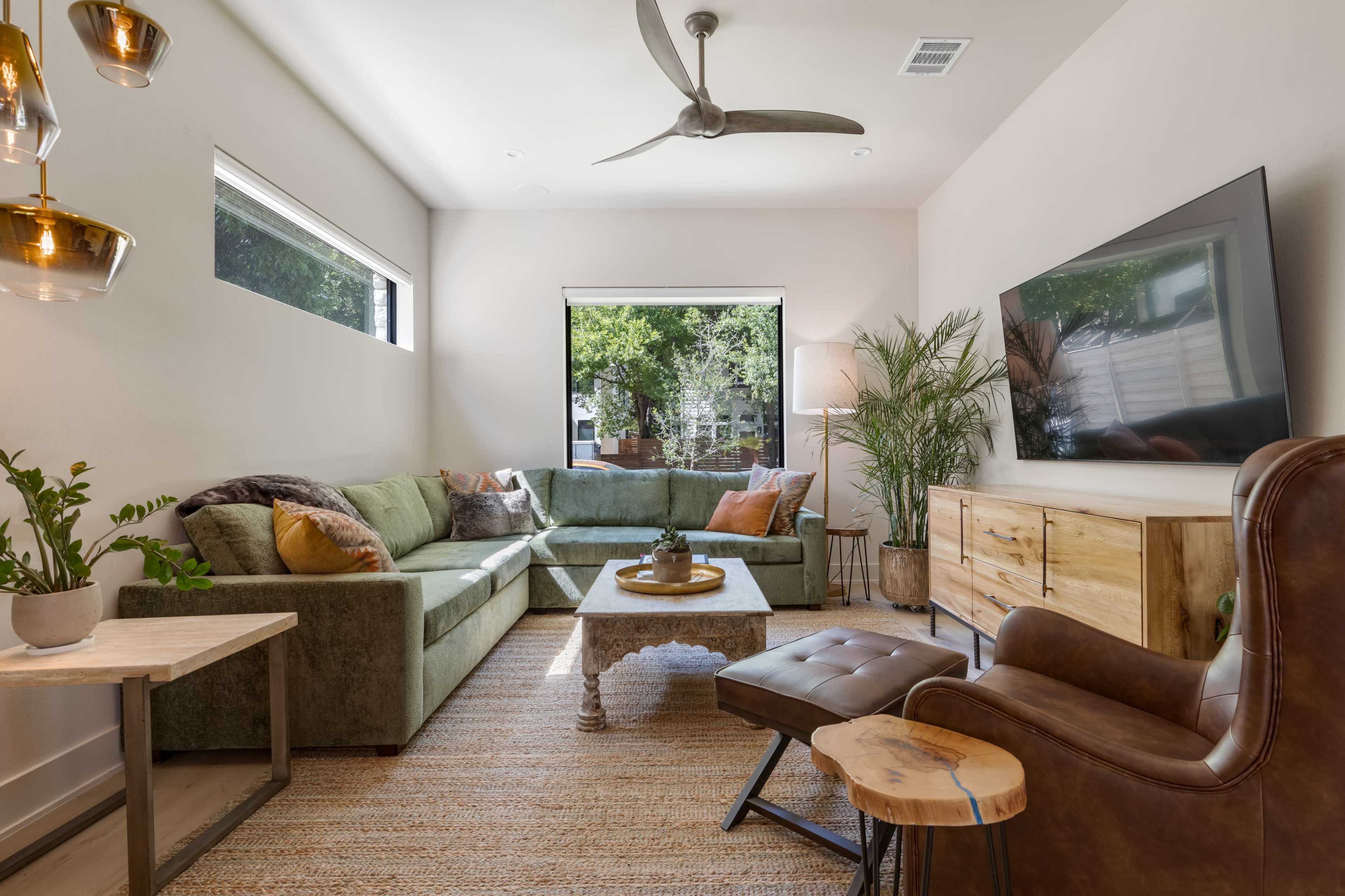 The living room features a green sectional sofa, a wooden coffee table, and a large window with a view of greenery.