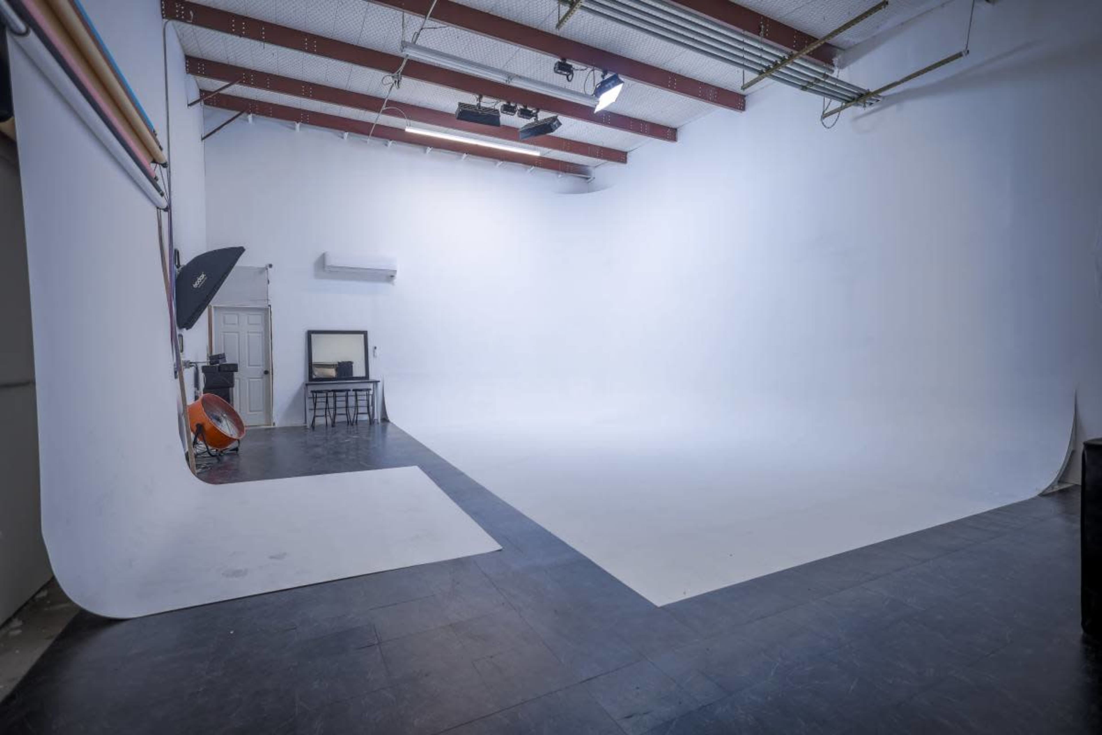The image shows a spacious photography studio with a seamless white backdrop and minimal furniture.