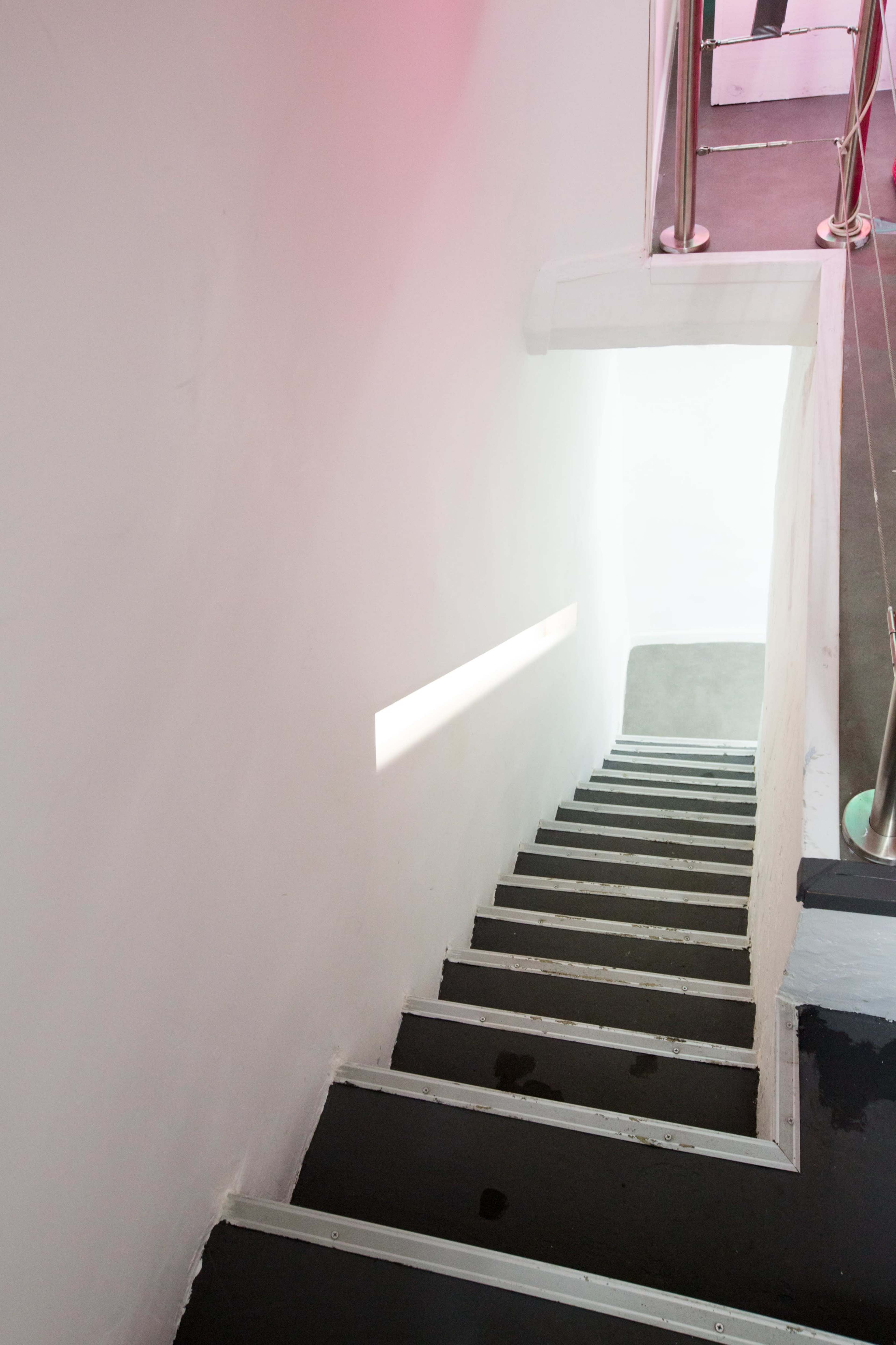 A staircase leads down into a well-lit space, with a beam of light illuminating the steps.
