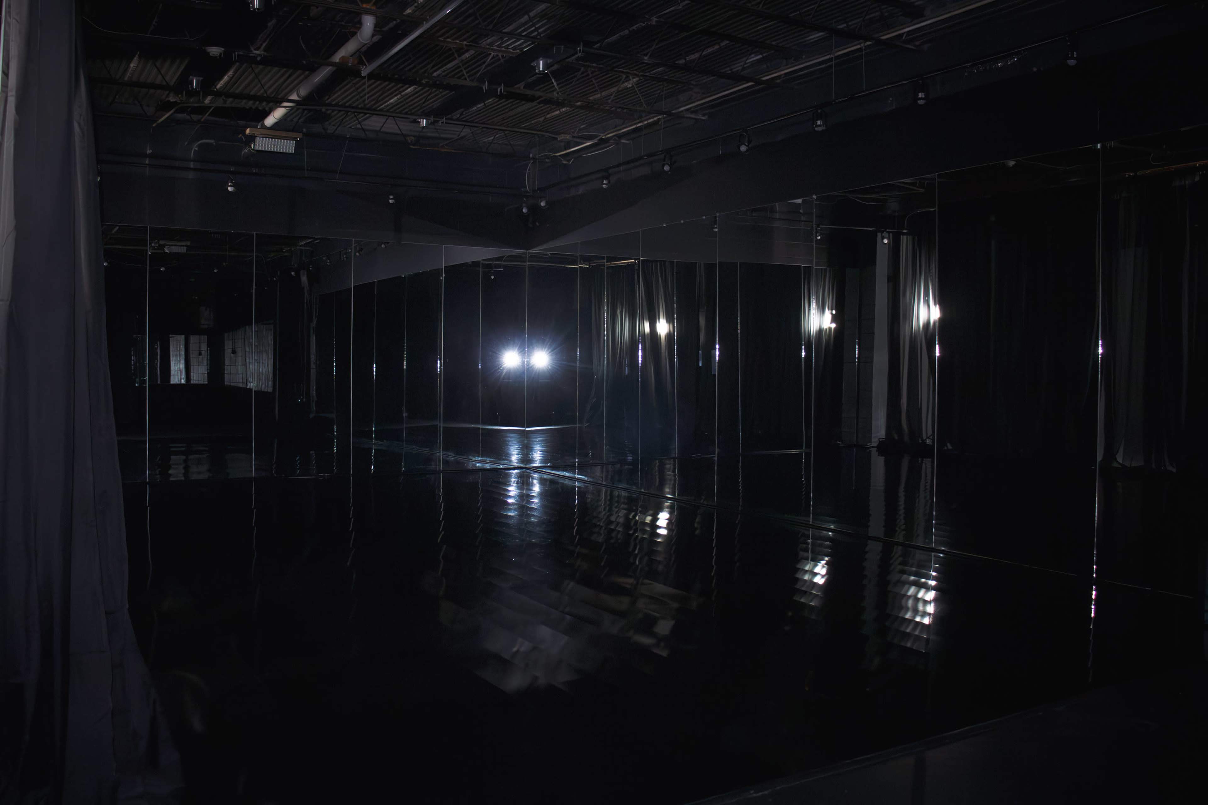 The image shows a dark room with mirrored walls reflecting lights and a polished floor.