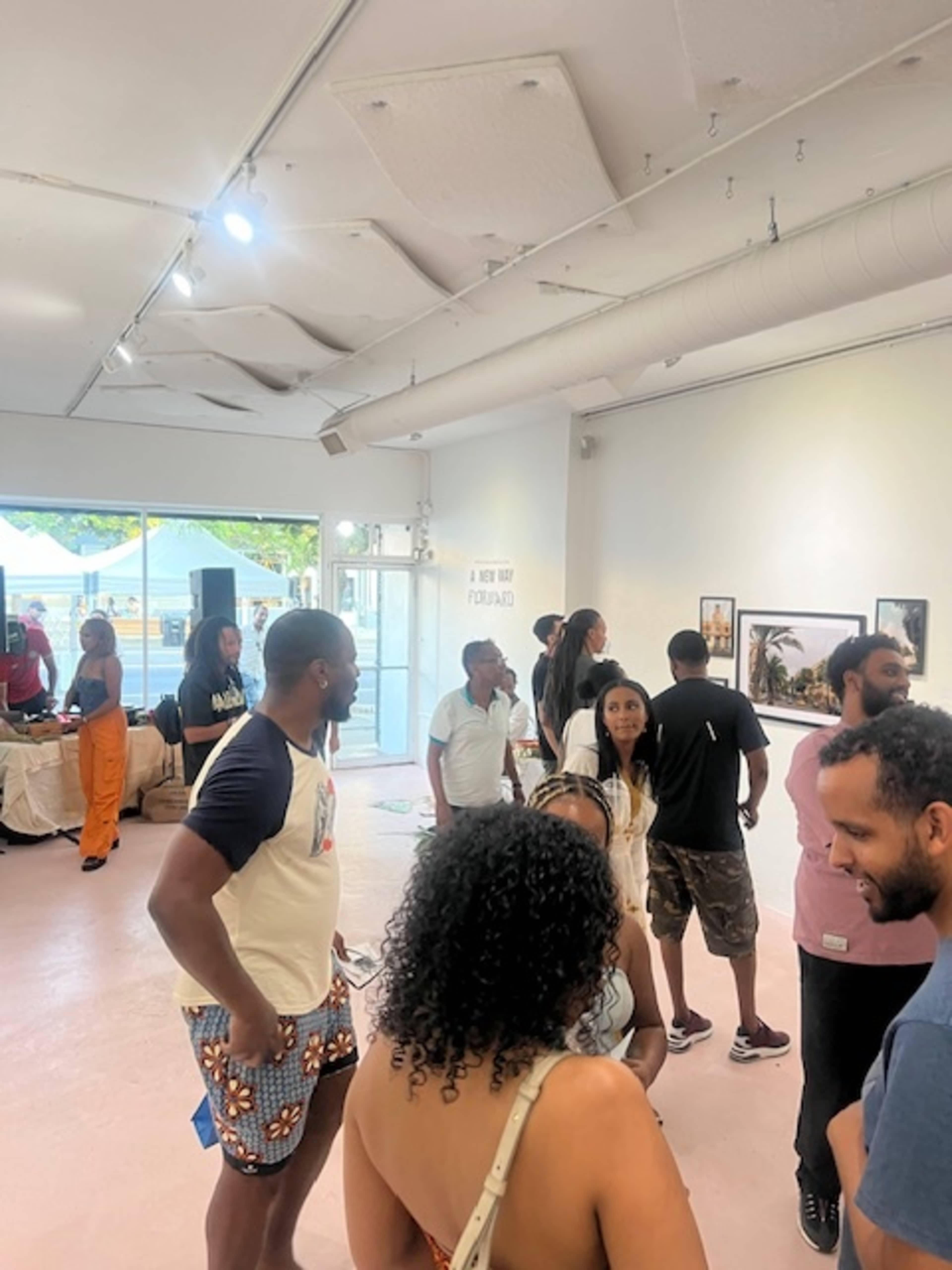 A diverse group of people gather and converse inside an art gallery filled with photographs.