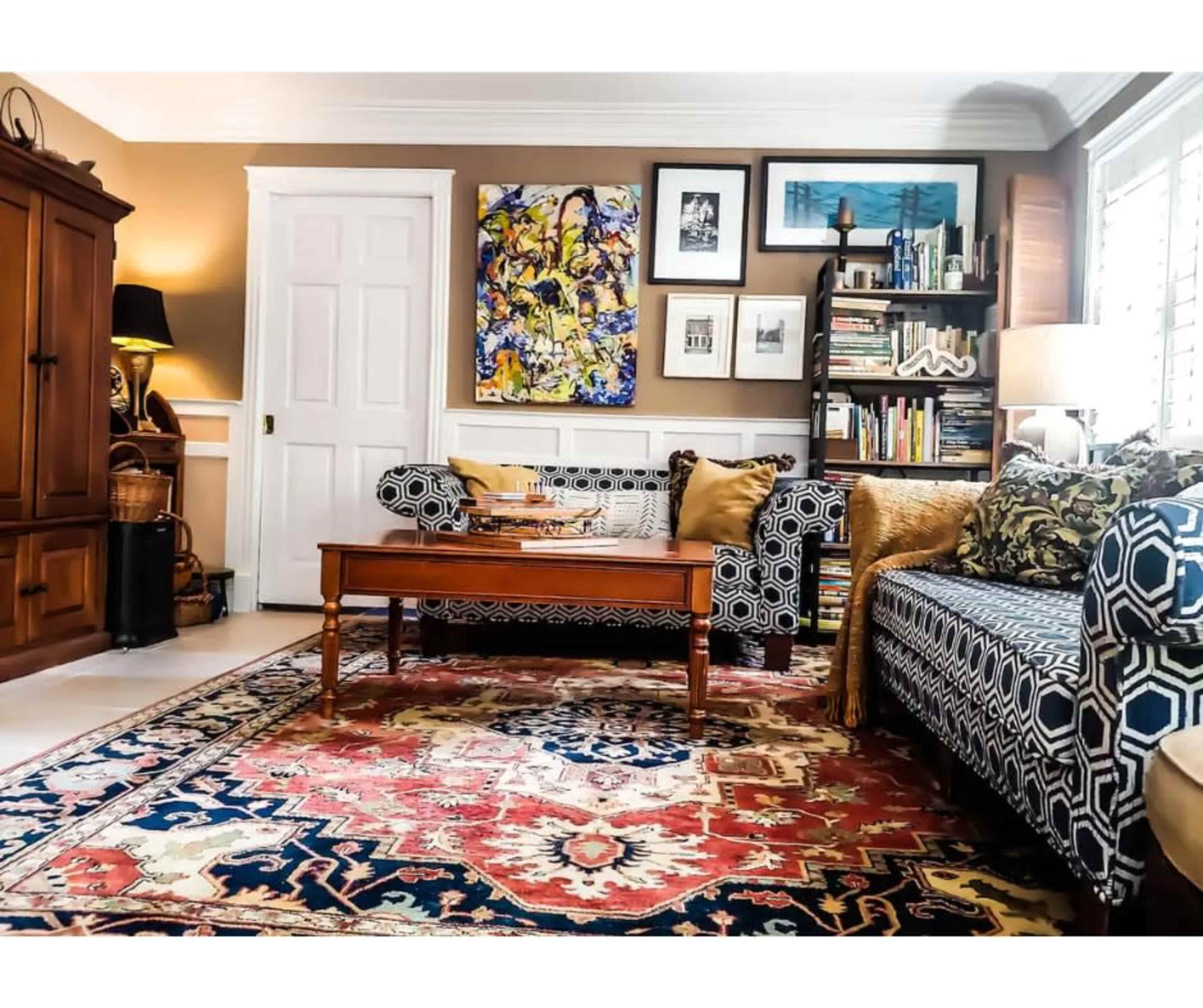 The living room features two patterned sofas, a wooden coffee table, a colorful rug, and bookshelves filled with books and decor.